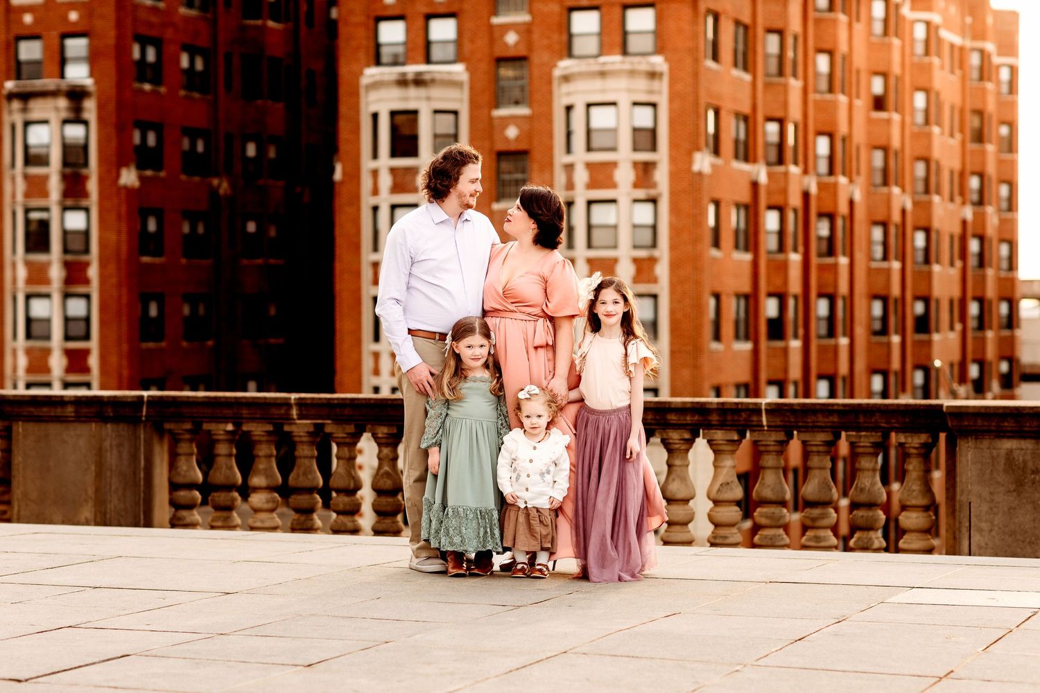 A family of five stands on a rooftop downtown Indianapolis Indiana with brick buildings in the background.