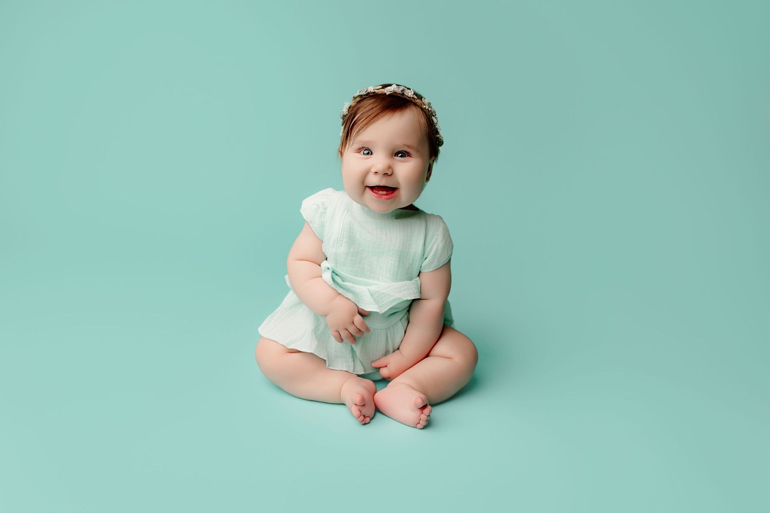 A joyful baby in a light blue dress sits against a matching background baby photography Indianapolis Indiana