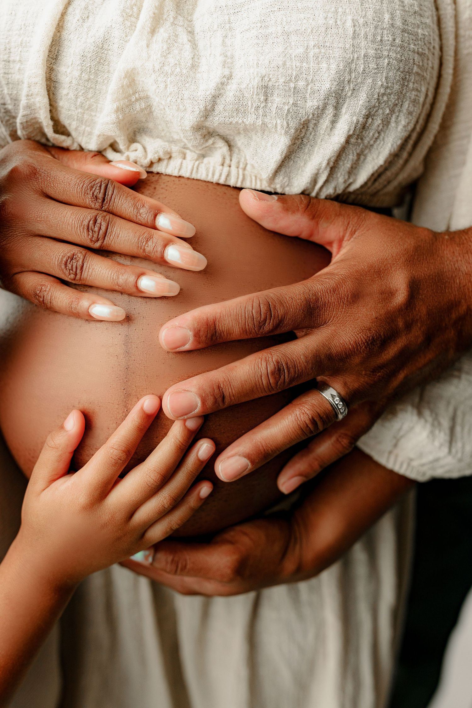 A close-up image of a pregnant belly with three hands gently resting on it—an adult male, adult female, and a child