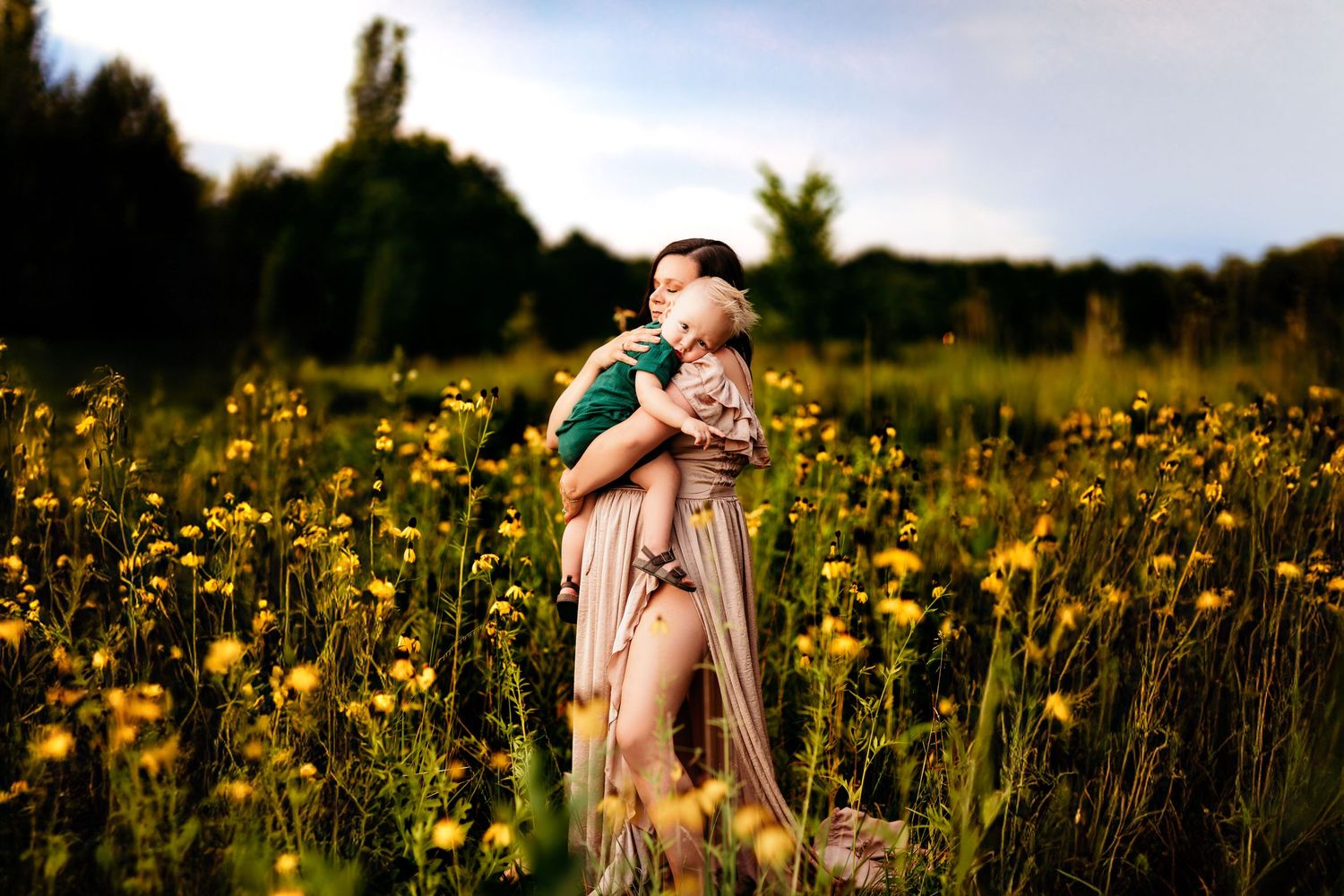 A woman in a flowing dress holds a child in a field of yellow wildflowers. The scene conveys warmth and serenity,