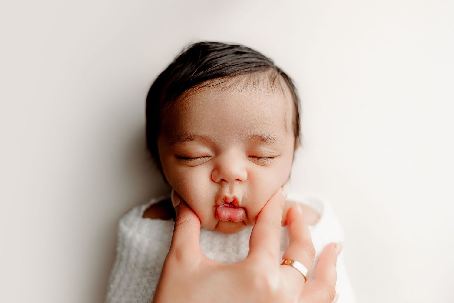 Wrapped newborn portrait with parent's hands in neutral tones Indianapolis studio