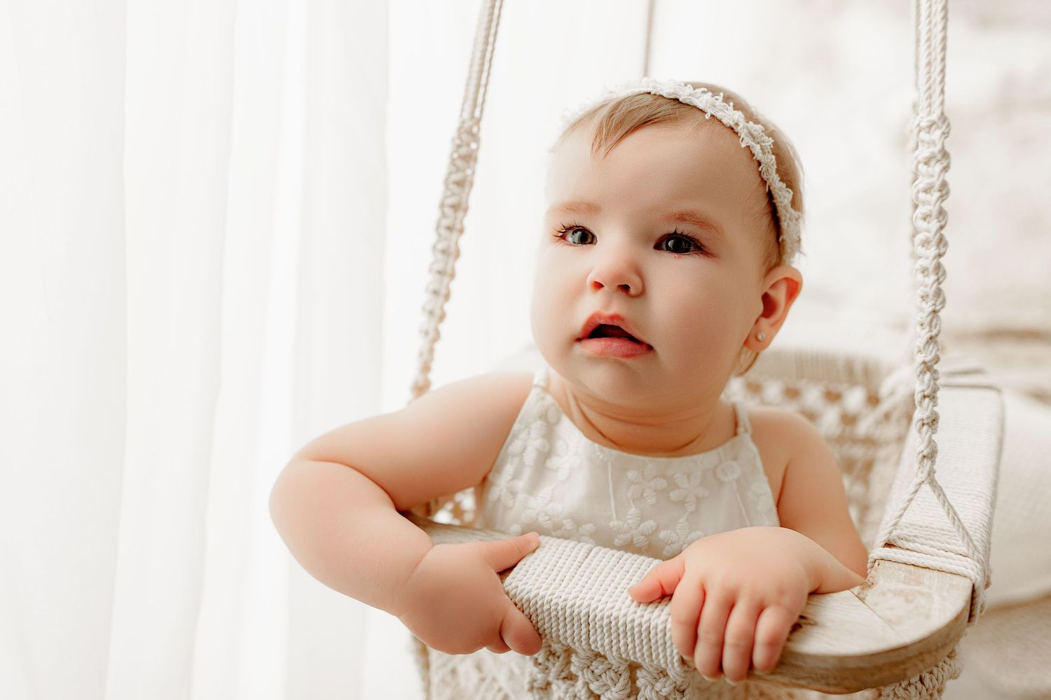 Baby girl in neutral lace outfit sitting in woven swing baby milestone portrait Indianapolis