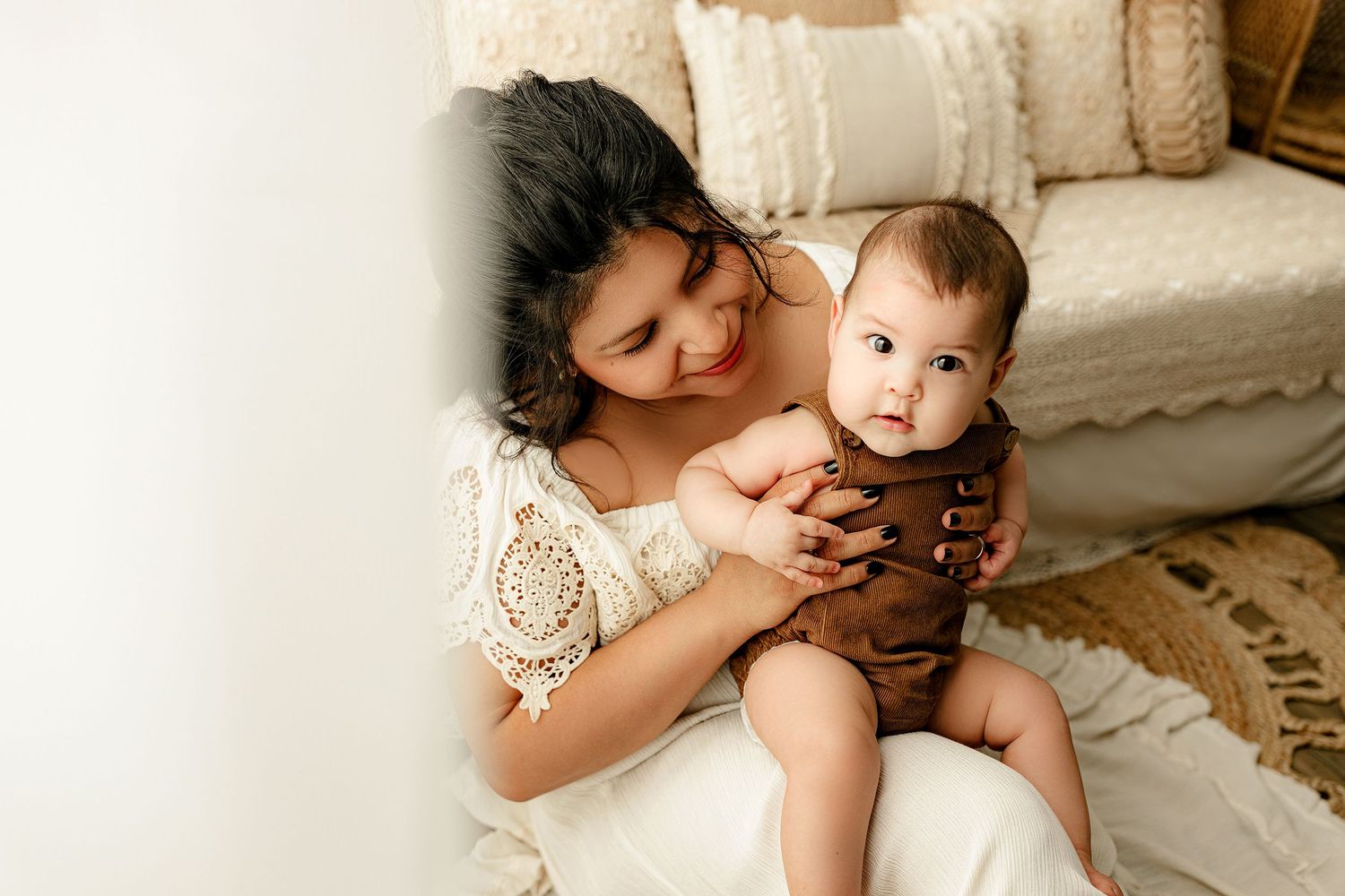 A woman lovingly holds a baby seated on her lap in a cozy room. She's smiling warmly, and the baby gazes curiously.