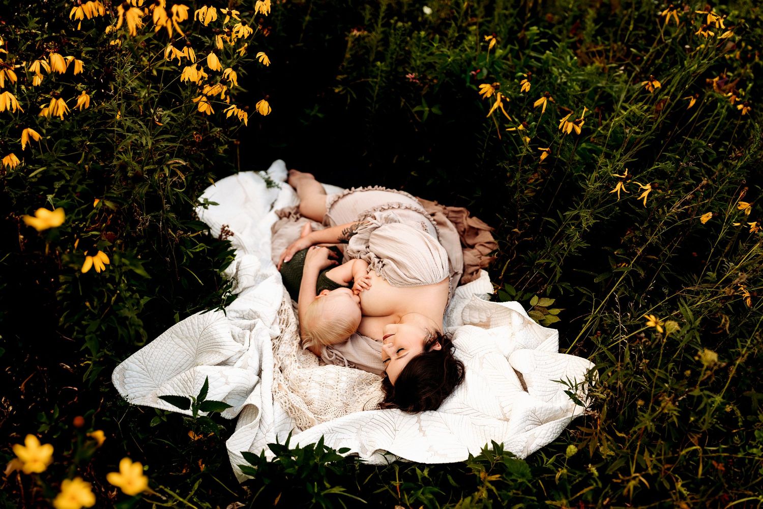 A mother and baby peacefully rest on a white blanket surrounded by lush greenery and yellow flowers, conveying love and connection