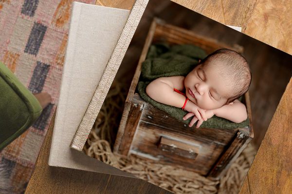 Two photo albums stacked, with the top showing a cover image with a baby posed in a brown wooden crate