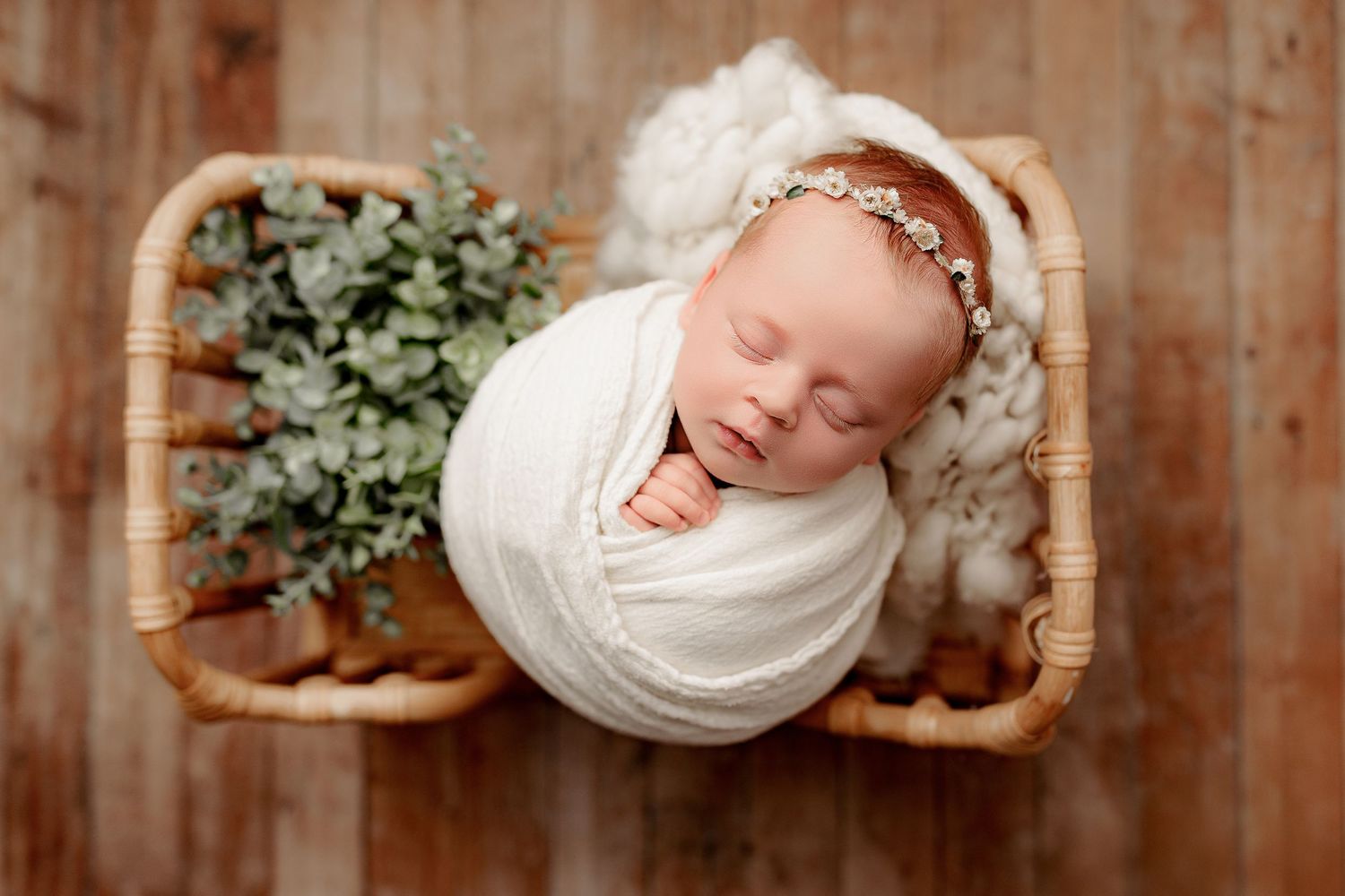 Baby girl swaddled in white posed in a wood prop in cozy newborn studio Indianapolis