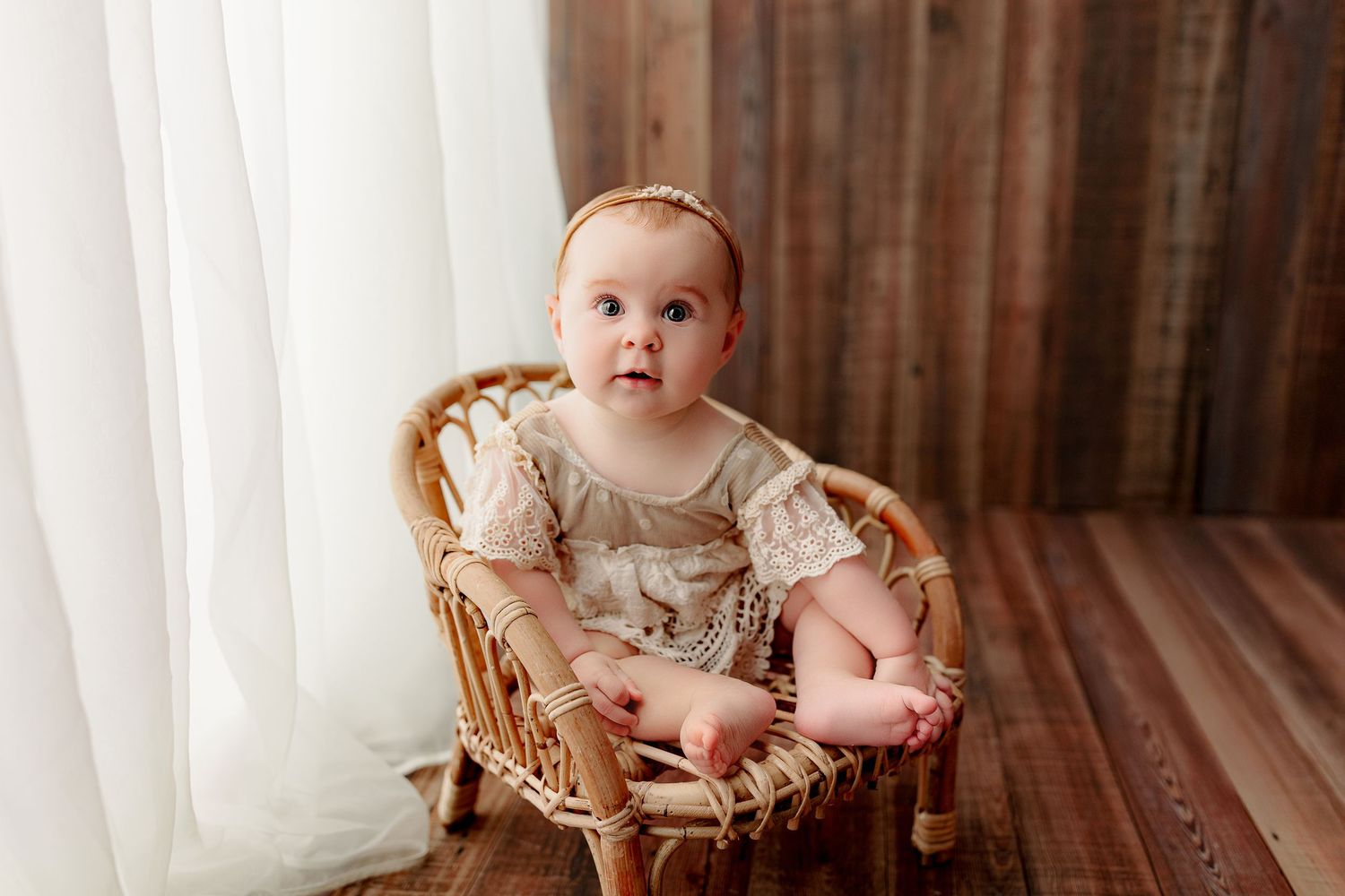 Indianapolis baby milestone photographer baby girl sitting in rattan chair with neutral outfit against wood backdrop