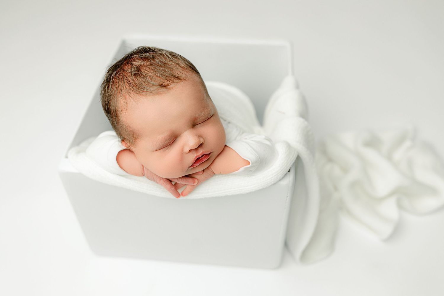 A peaceful newborn sleeps in a white box wrapped in a soft blanket, exuding warmth and innocence.