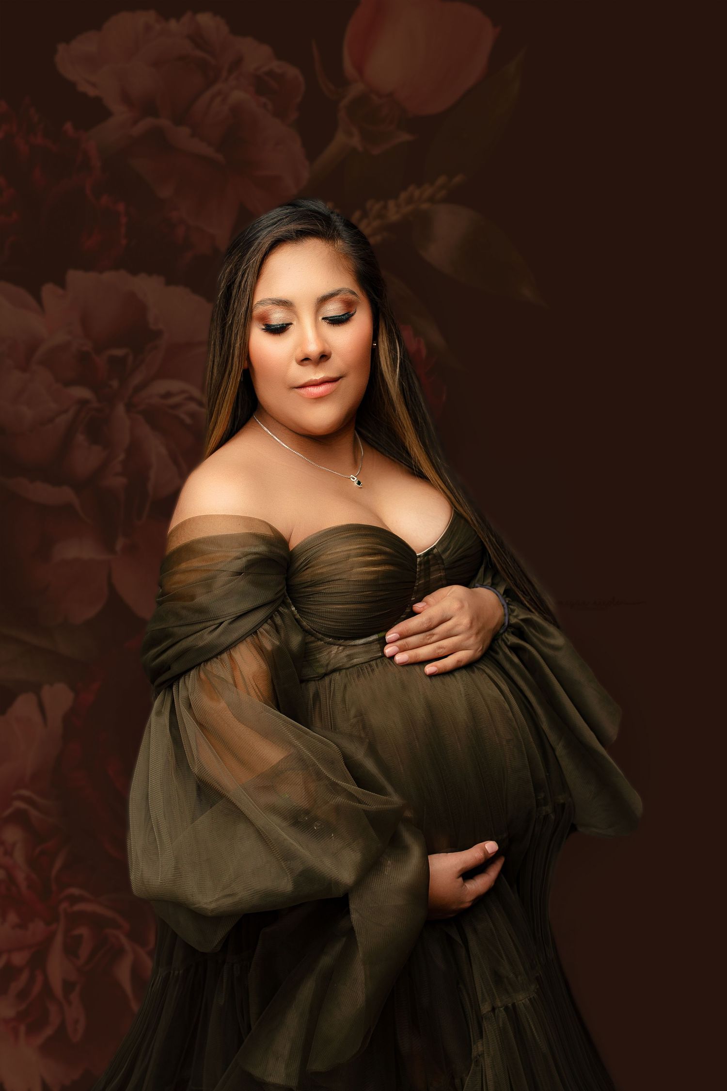 Pregnant woman in a flowing olive gown cradles her belly, set against a floral brown background. She appears serene and peaceful.