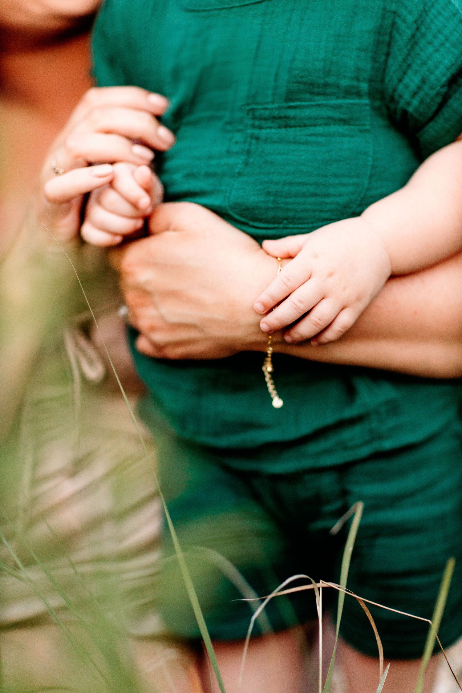 A toddler in a green outfit is held closely by an adult, who gently holds the child's hands. The scene is warm and tender