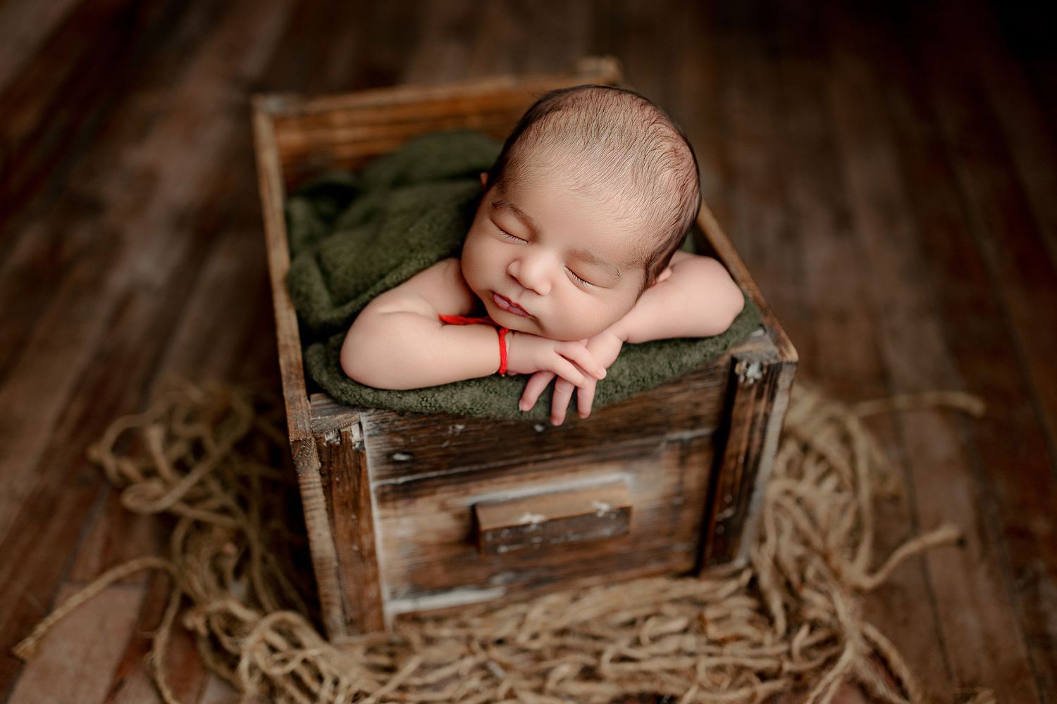 Sleepy baby boy posed in crate on wood backdrop with Indianapolis Newborn Photographer