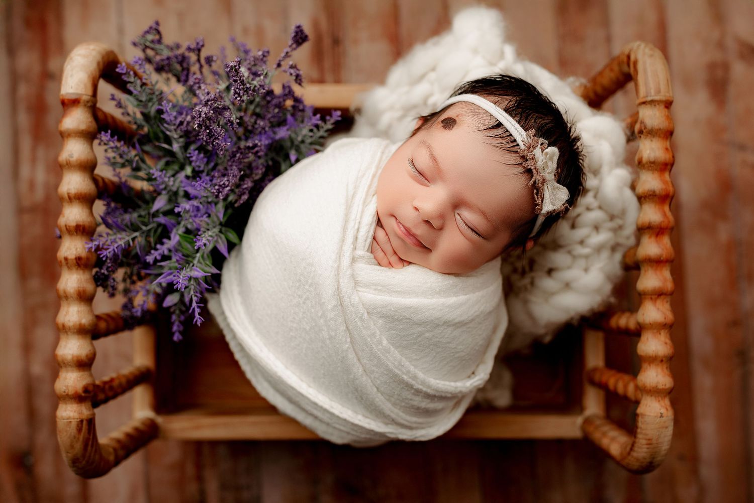 Baby girl posed on tiny bed with florals and swaddled newborn session Indianapolis