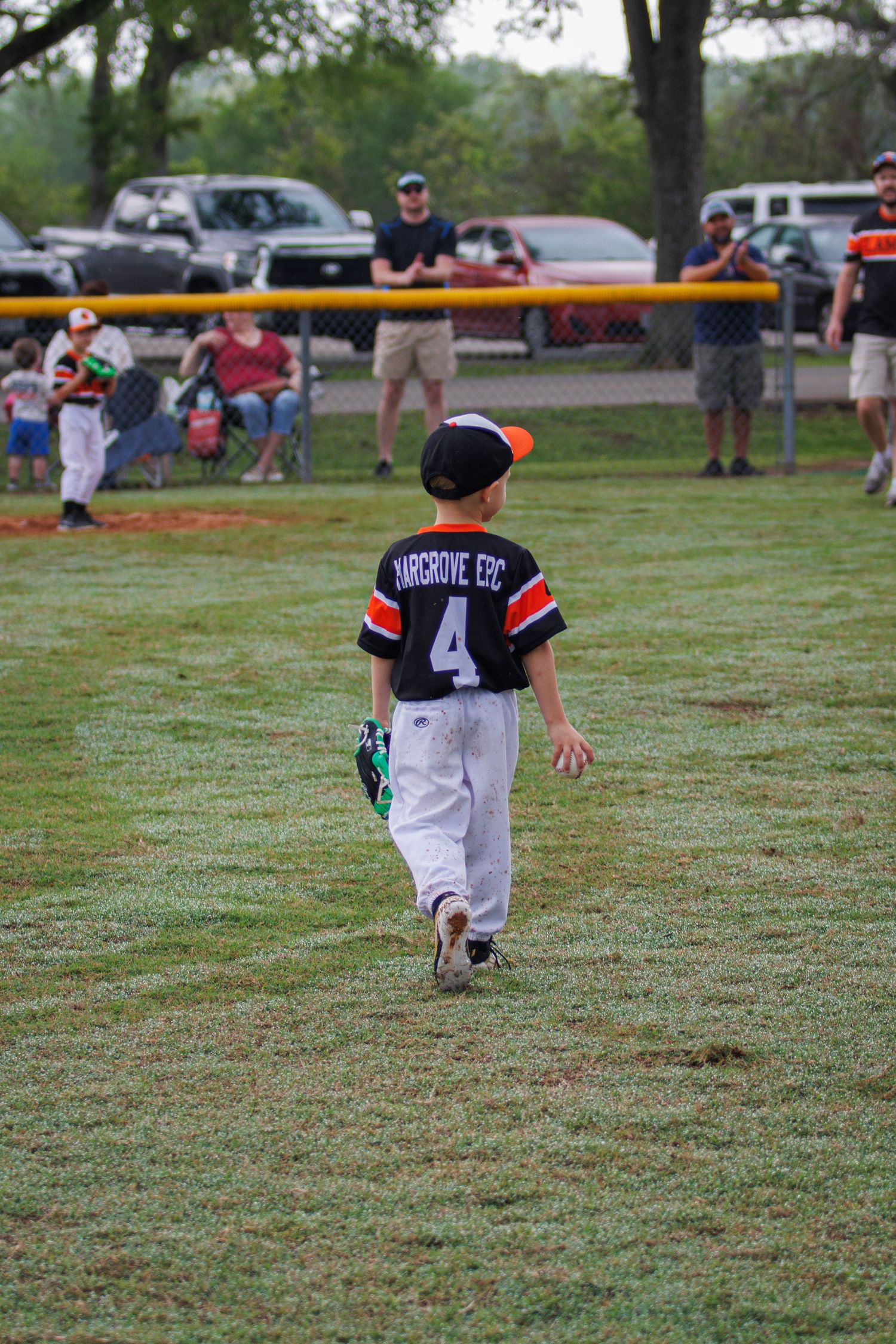 Young baseball player wearing jersey number 4 walks on grass field during youth league game in Richmond, TX.