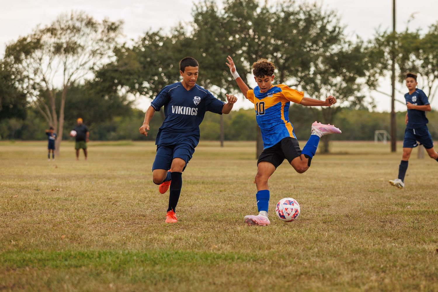 Soccer players compete for the ball during a match on a grass field in blue and orange uniforms.