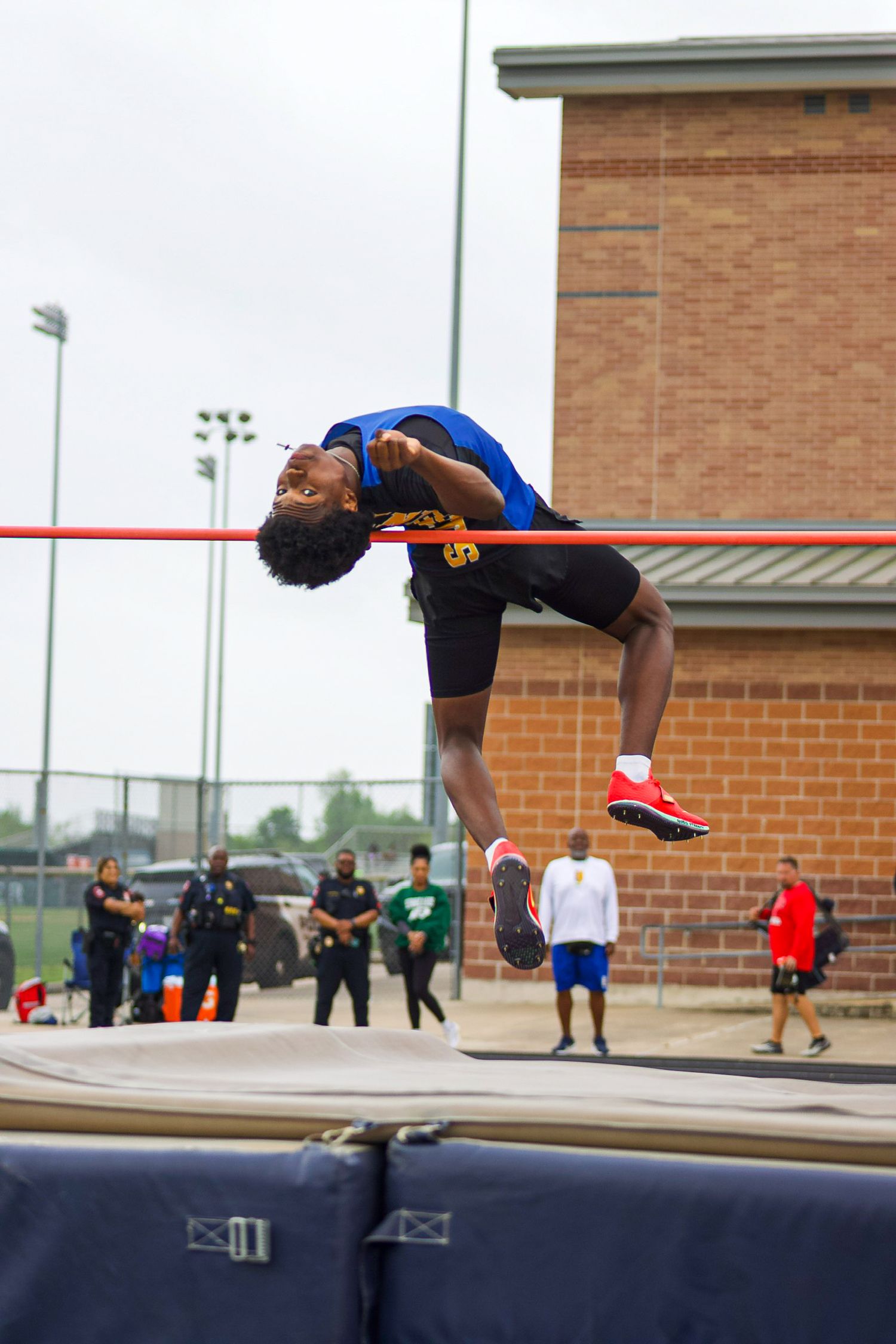 Elkins High School athlete executing high jump technique over bar during district track meet in Missouri City, TX.