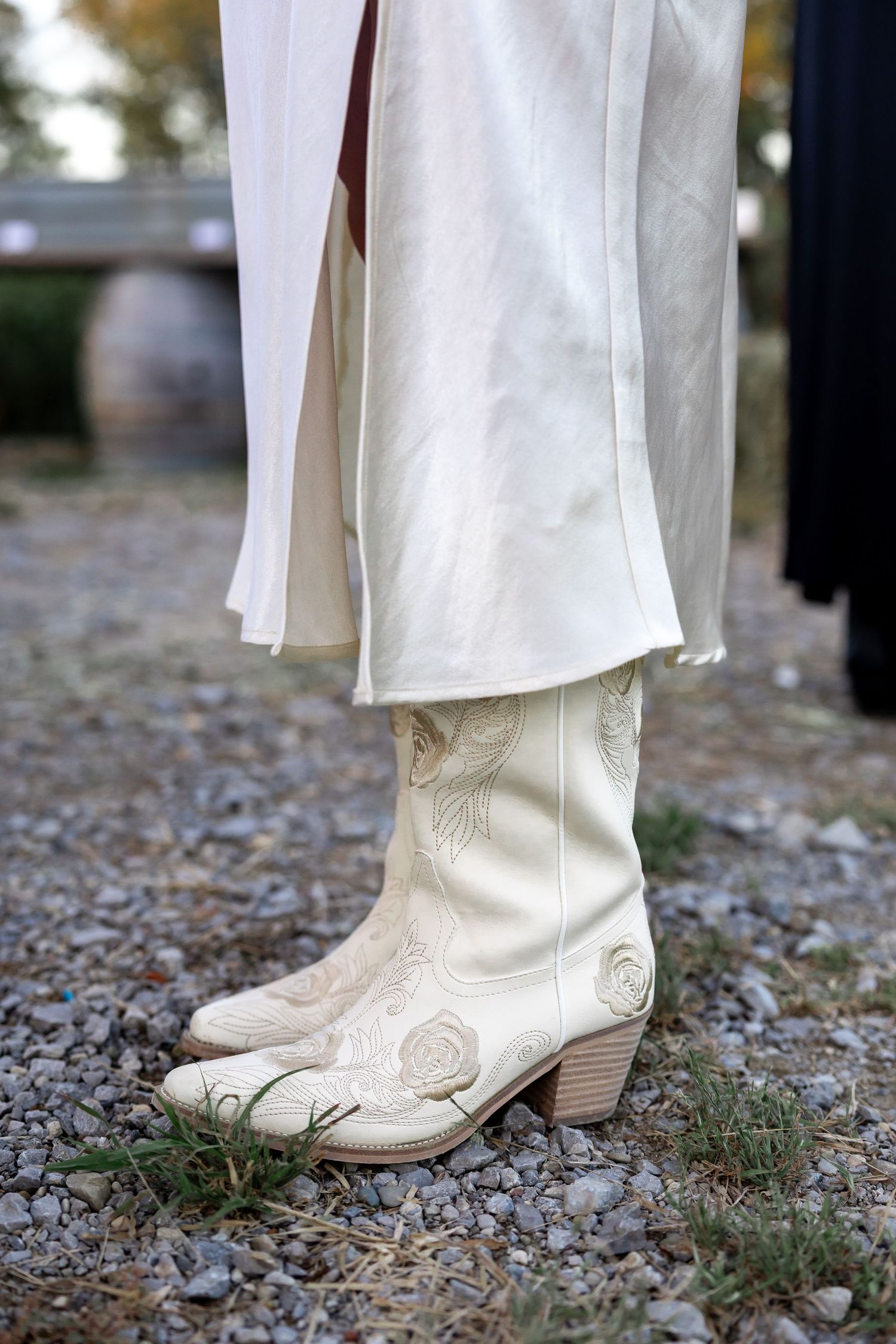 White cowboy boots with decorative stitching shown against gravel ground.