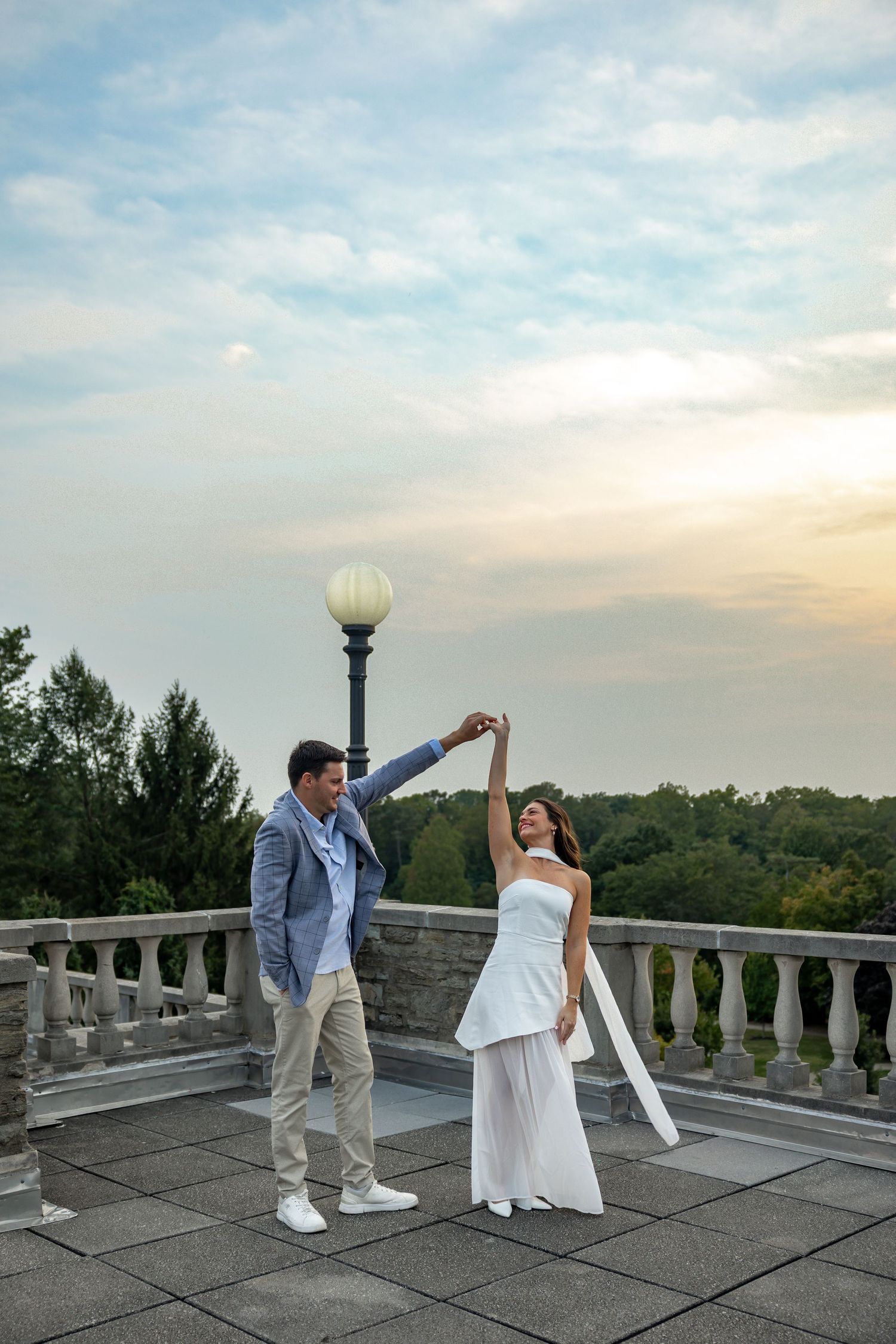 A couple dancing and twirling on a stone terrace during golden hour.