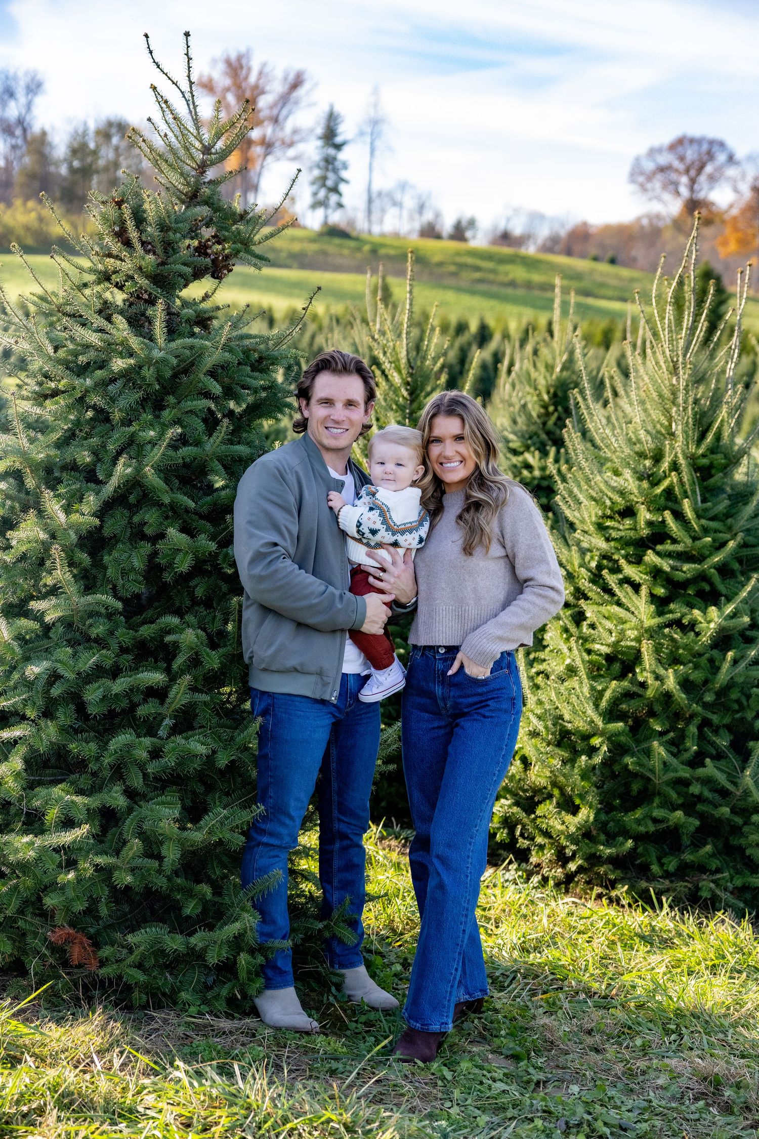 Family posing together at a Christmas tree farm on a sunny autumn day.