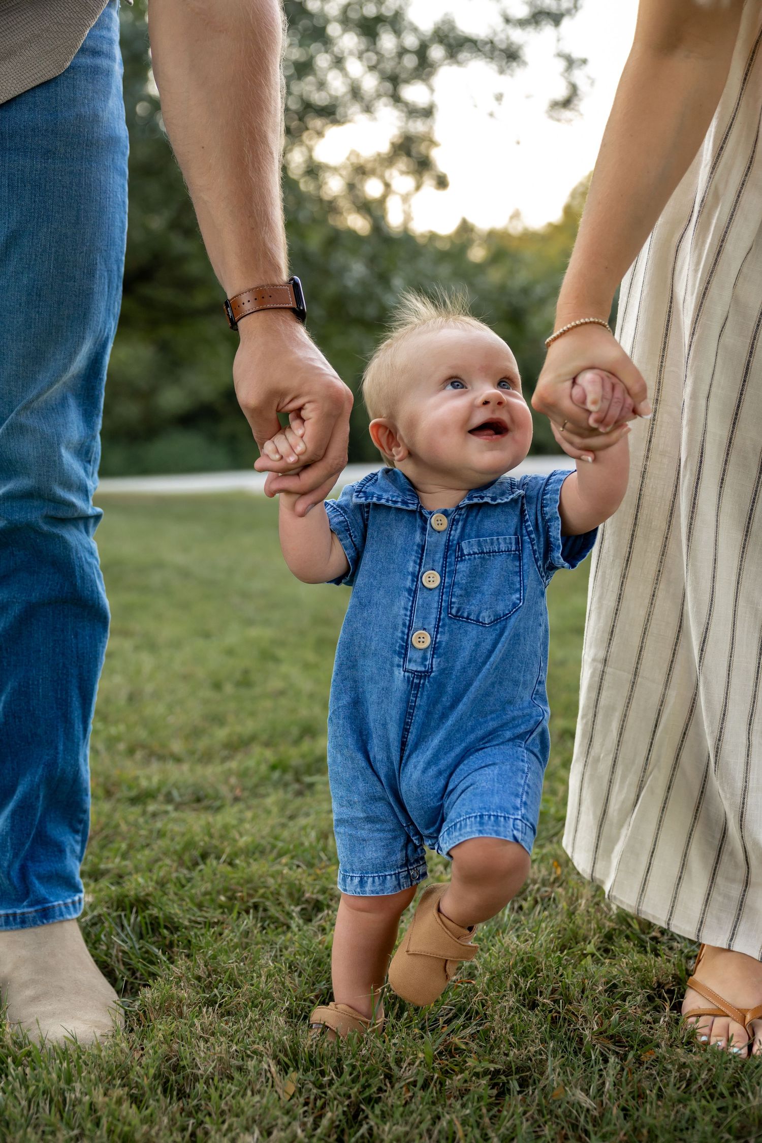 Close-up of baby feet in denim overalls taking first steps while holding hands.