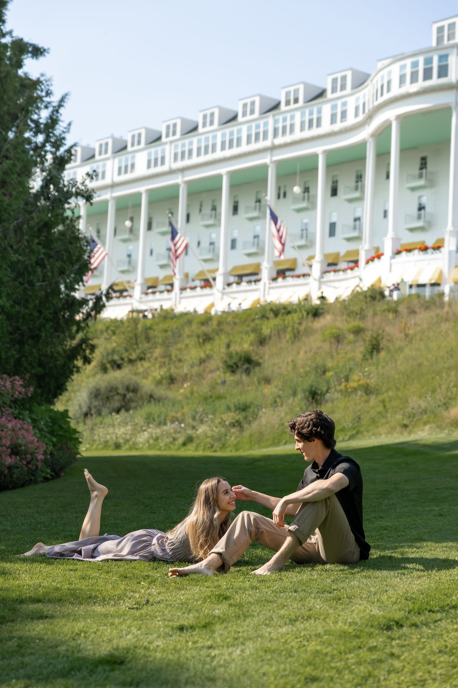 Two people relaxing on grass in front of a white colonial-style hotel building.
