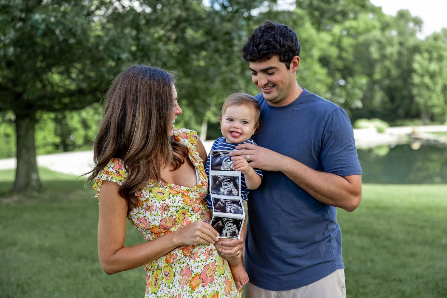 Family looking at a photo together while standing on grass in a park setting.