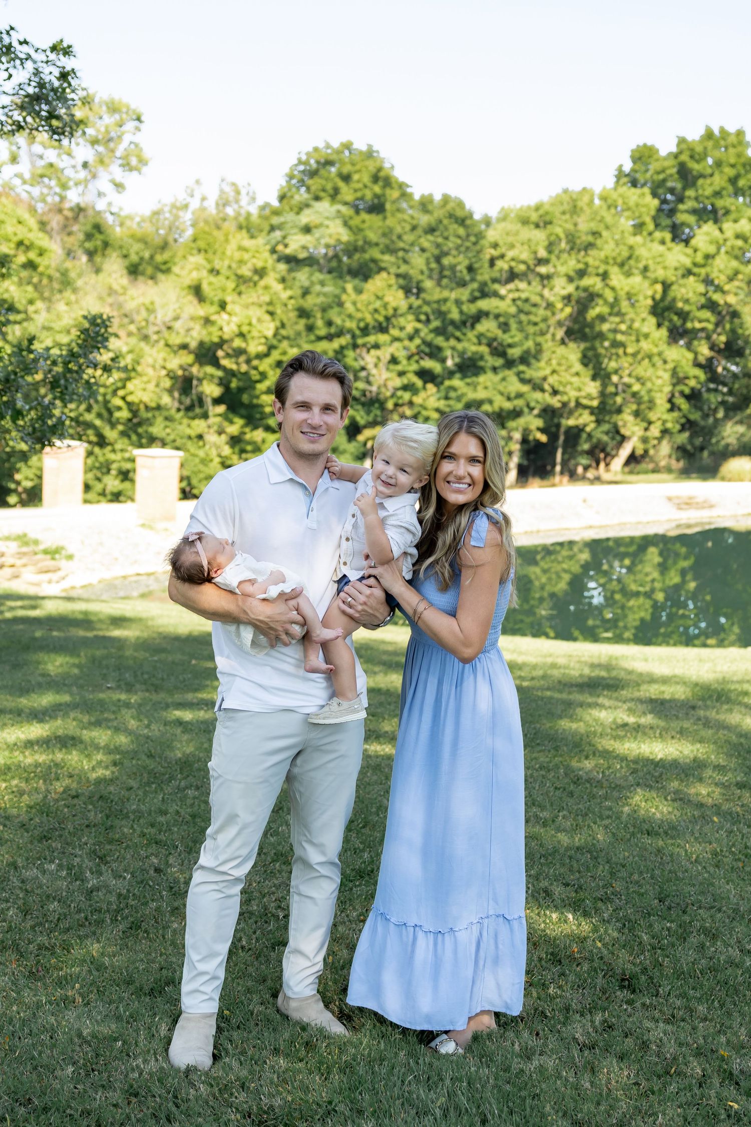 A family poses together on a grassy hill during a sunny outdoor photo session.
