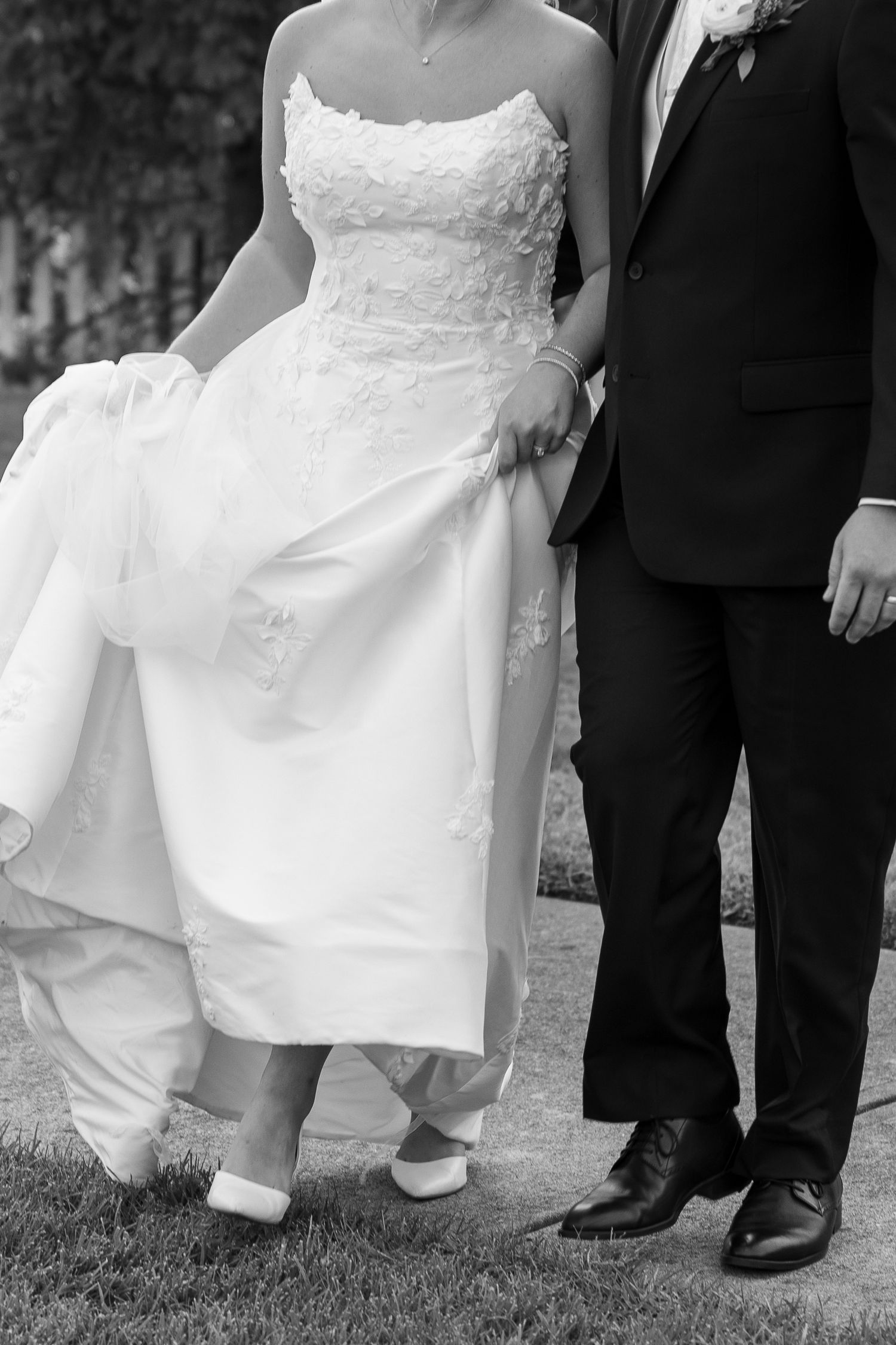Close-up detail shots of a bride's white wedding dress and groom's black shoes on grass.