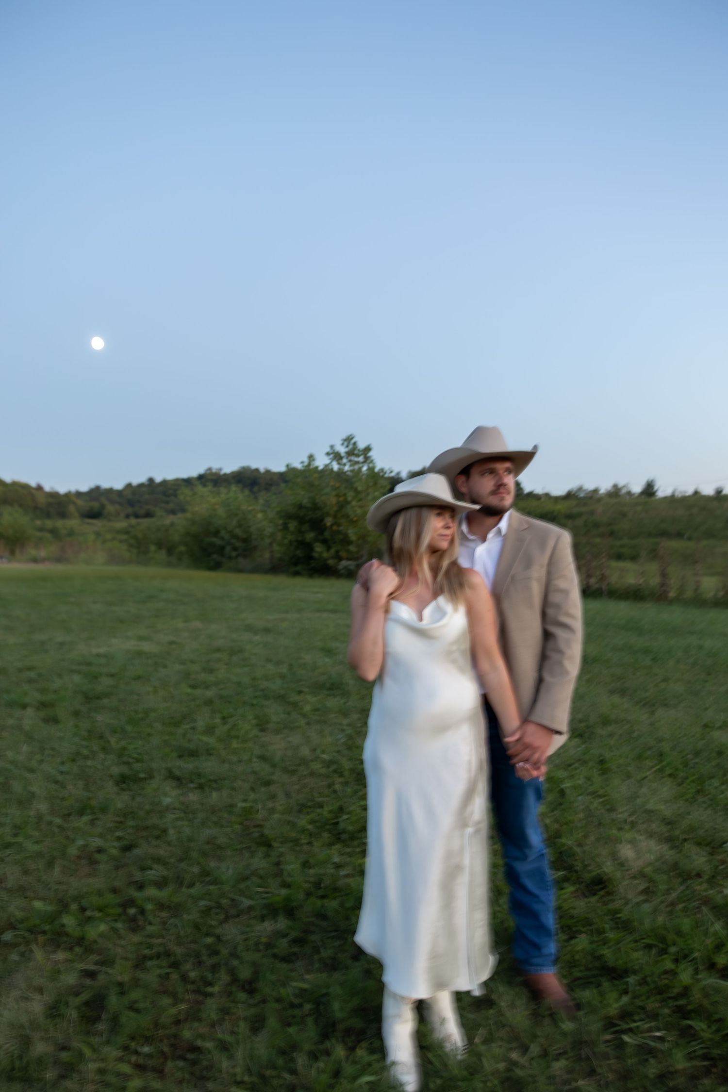 Two people share a romantic moment in an open field under blue skies.