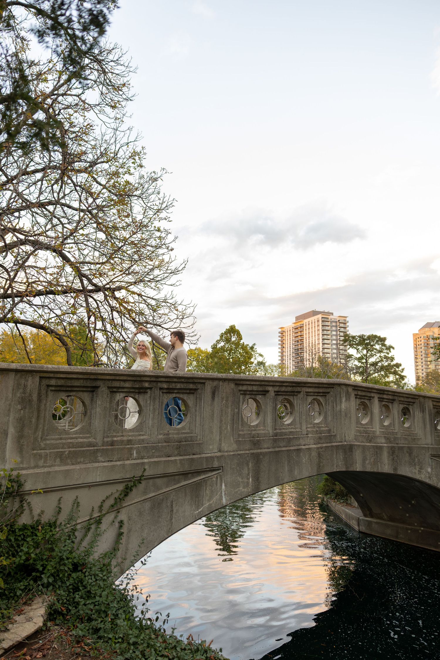 Stone bridge over water at sunset with city buildings in background.