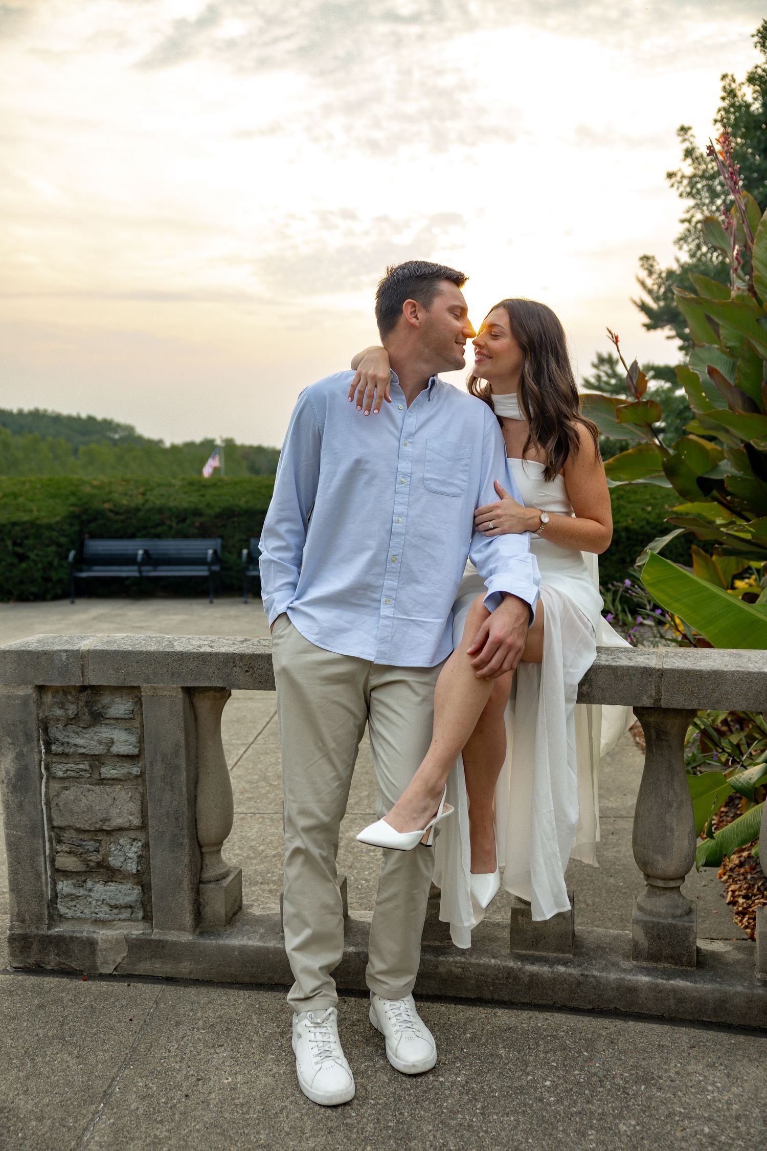A couple in white and light blue outfits sharing intimate moments by a stone balustrade.