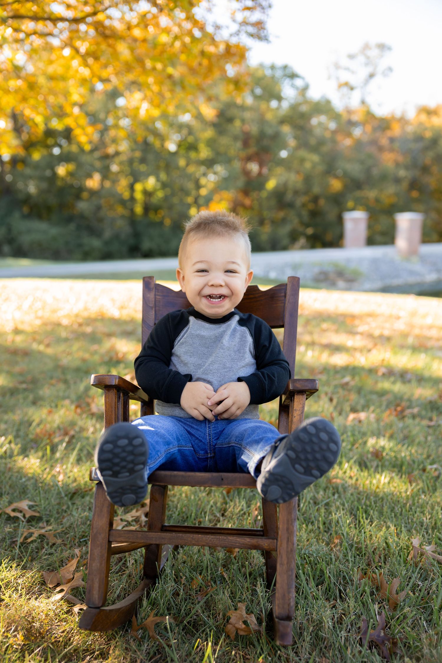 A child laughs while sitting in a small wooden chair on grass during sunset.
