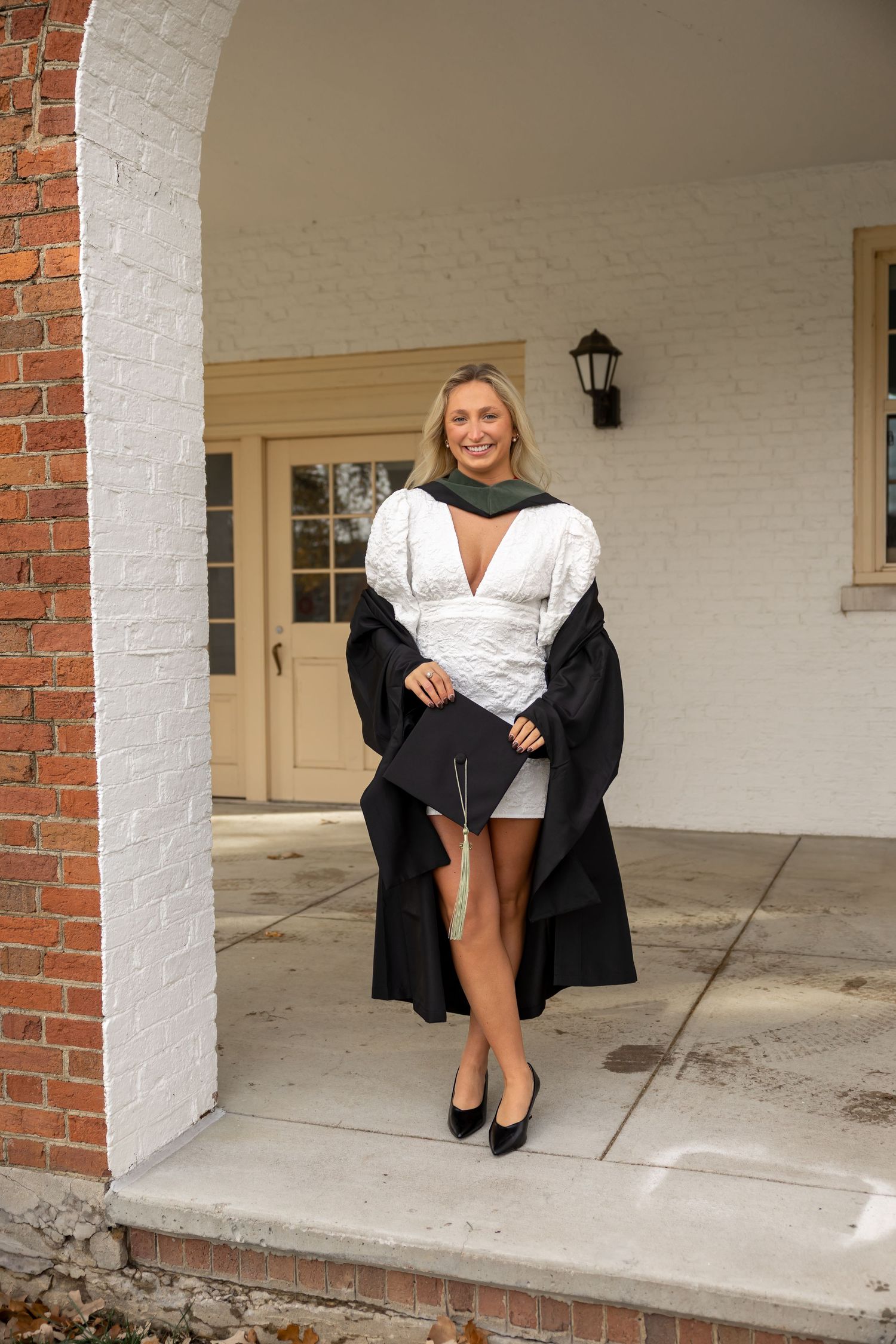 A person in a black jacket sits on a covered porch with white brick columns.