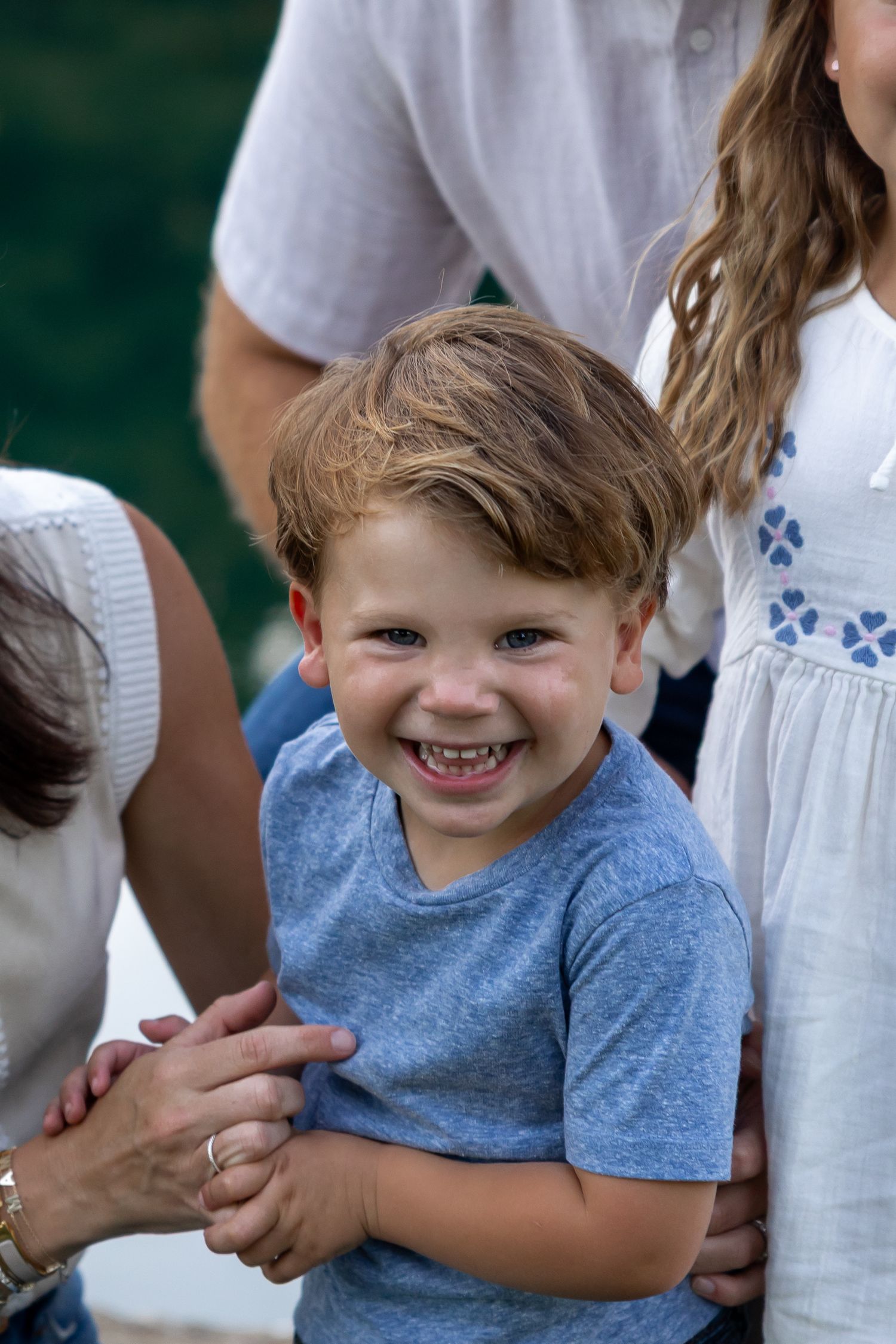 Child in blue t-shirt smiles joyfully during outdoor family photo session.