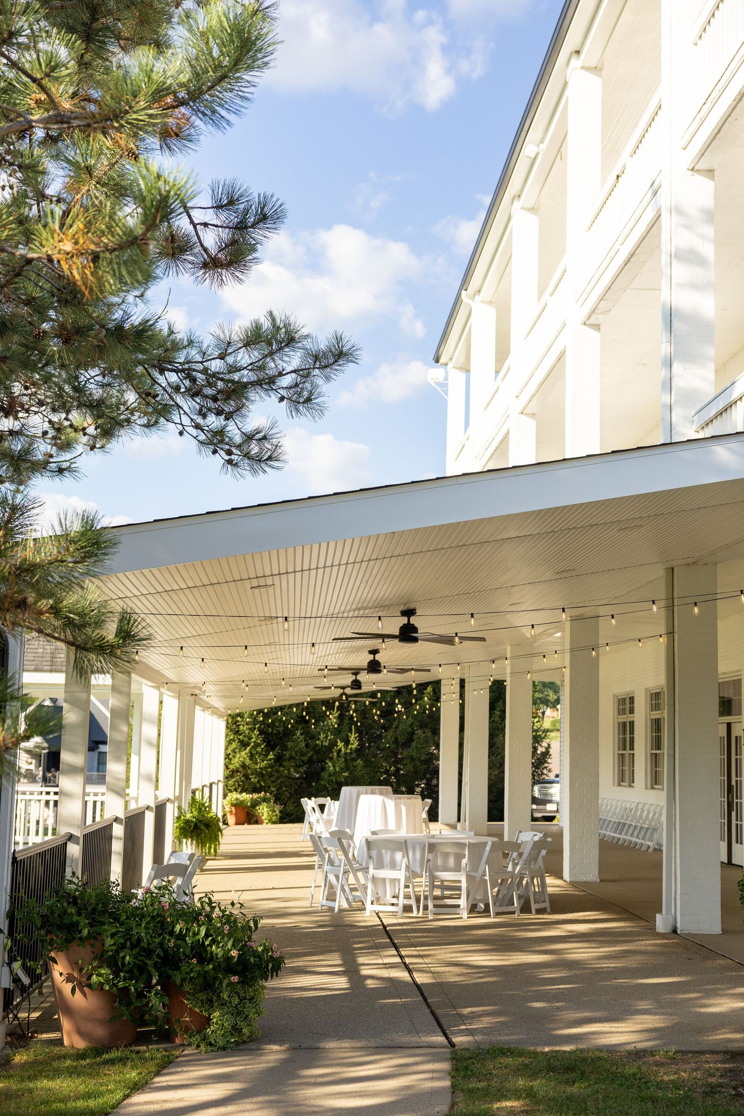 Long covered outdoor patio with white columns and string lights overhead.
