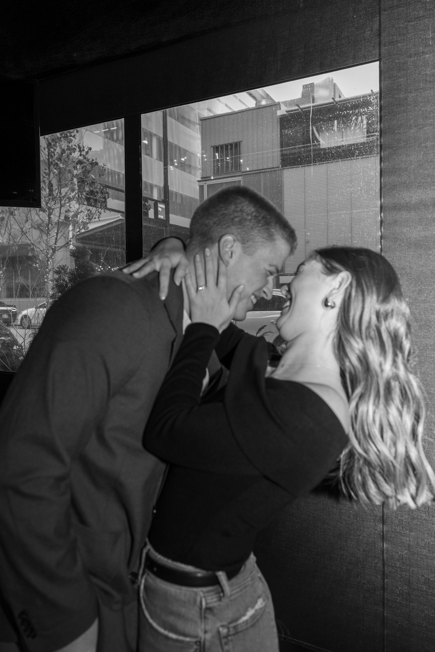 Black and white romantic moment captured against urban brick wall background.
