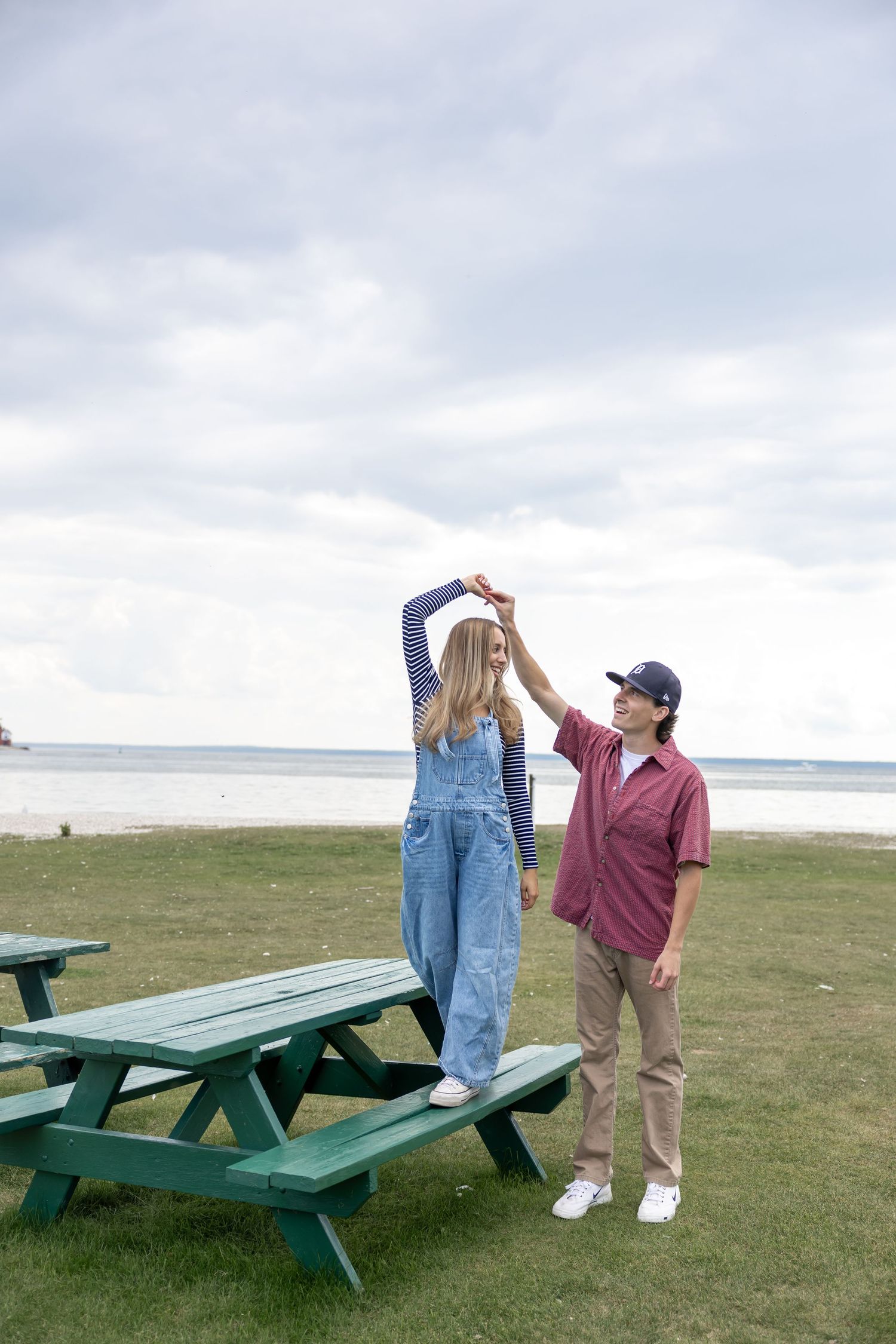 Playful interaction between two people near a green picnic table by the ocean.