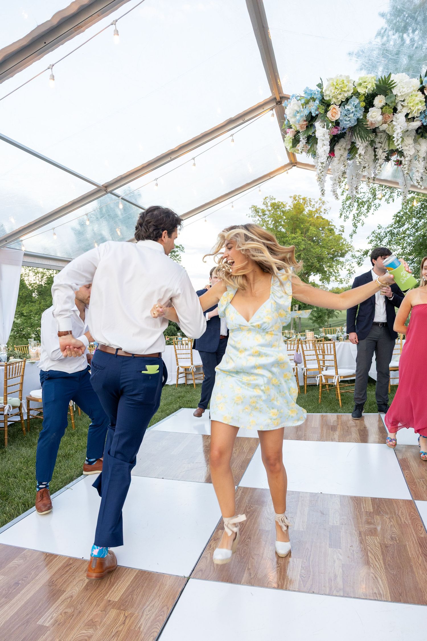 Couples dancing together on a wooden floor under a white tent at an outdoor wedding reception.
