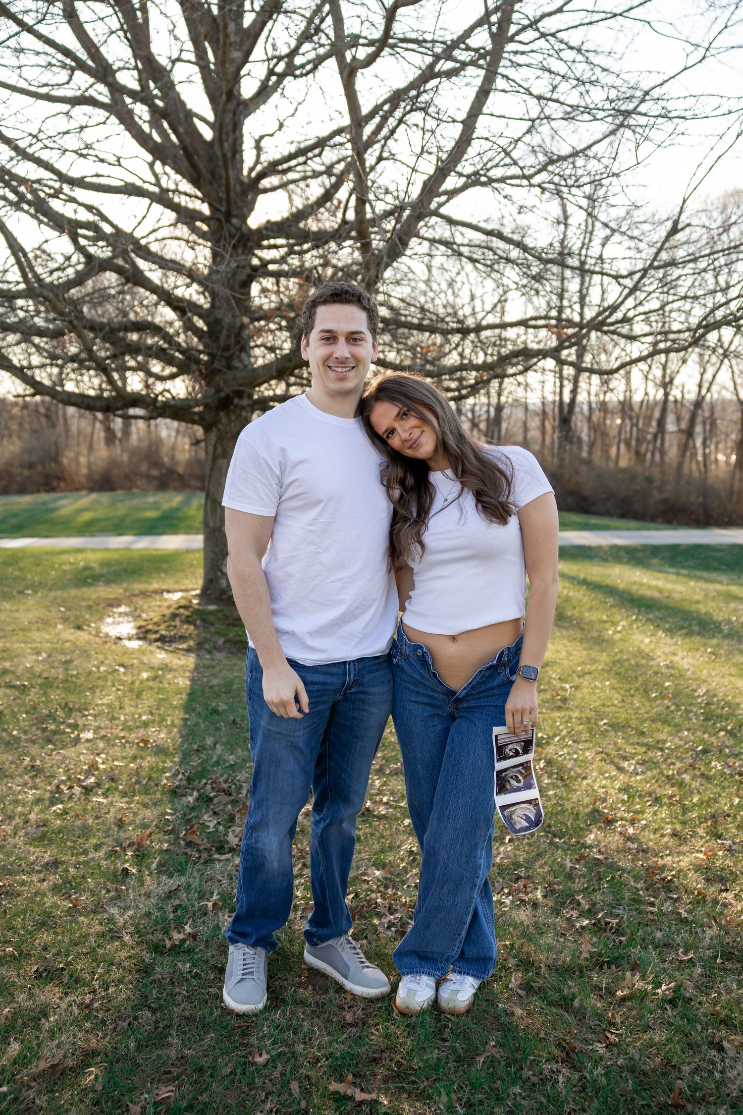 Outdoor photo session in a grassy field with bare trees in background.
