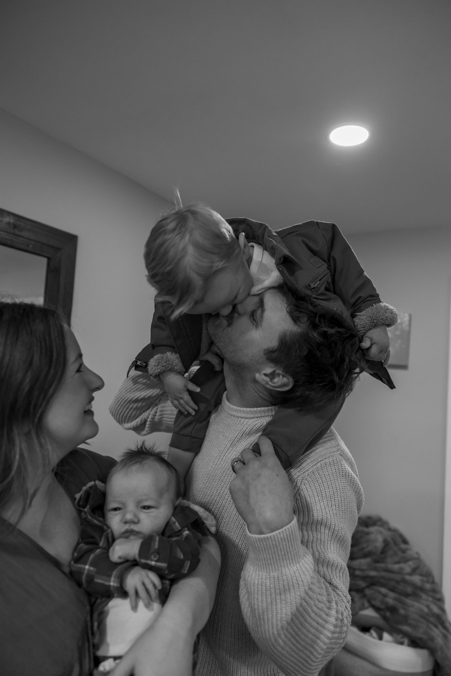 Family sharing playful kisses and laughter in a cozy indoor setting.