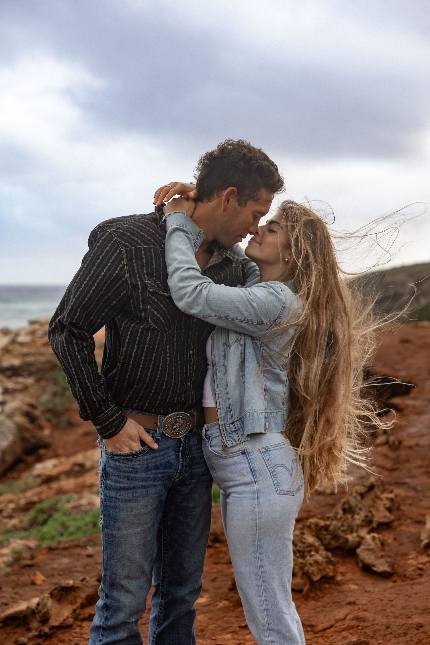 Romantic couple sharing kisses against a dramatic red rock landscape.
