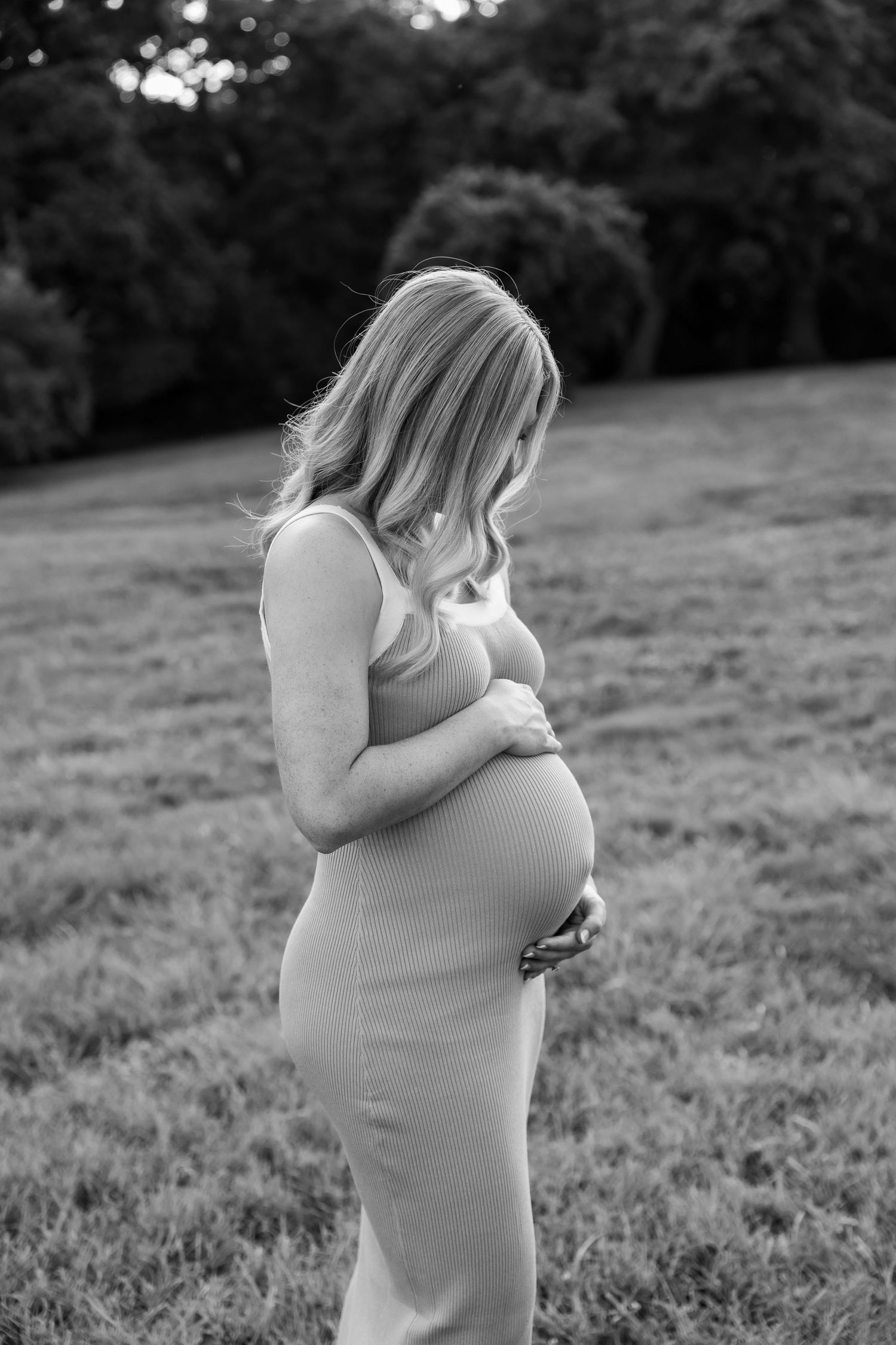 Black and white maternity portrait in outdoor setting with bokeh background.