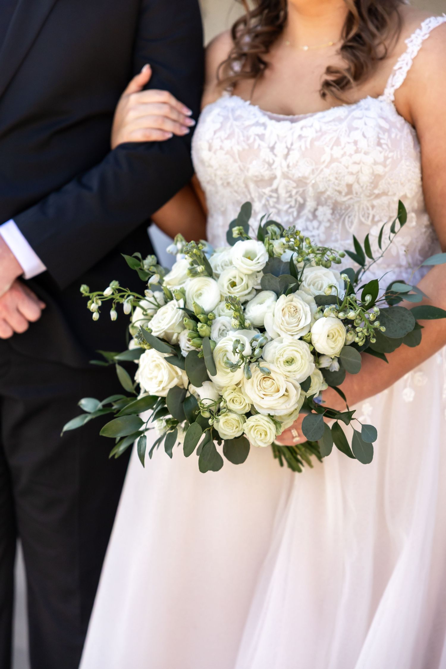 Wedding party members holding white rose bouquets against formal attire.