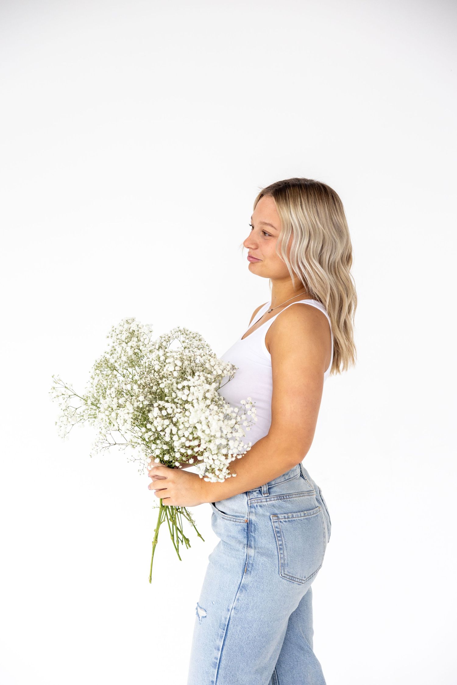 Side profile of woman holding delicate baby's breath flowers against white studio background.