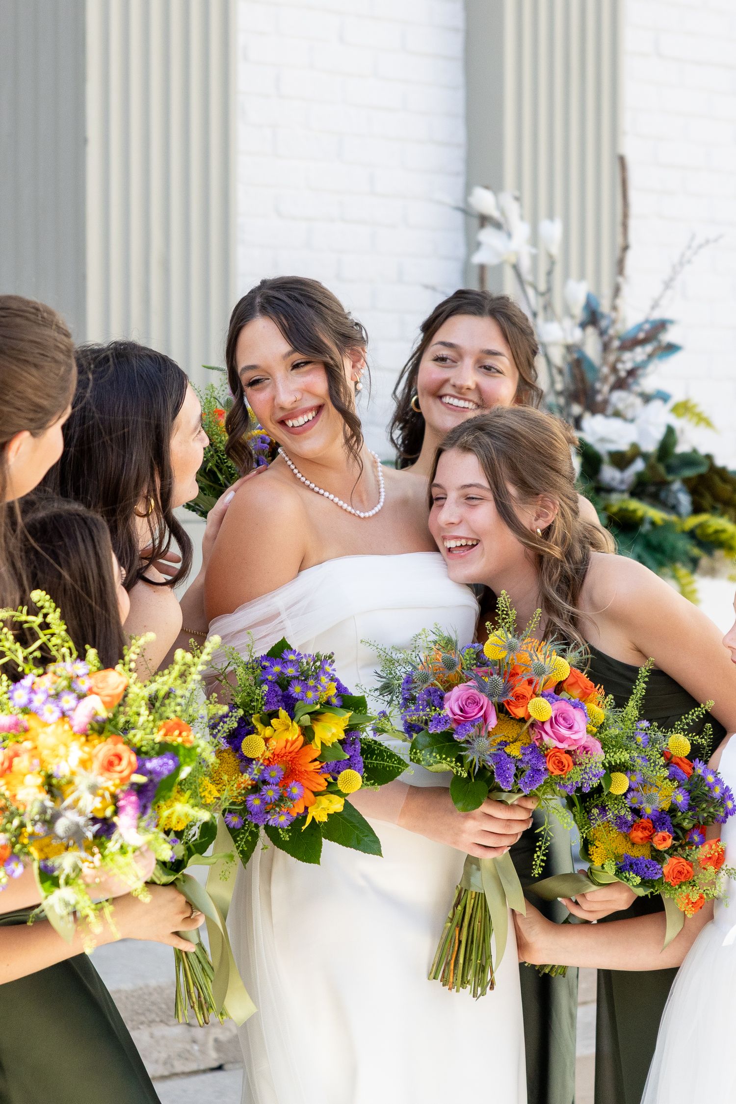 Wedding party holding vibrant multicolored bouquets against white columns.