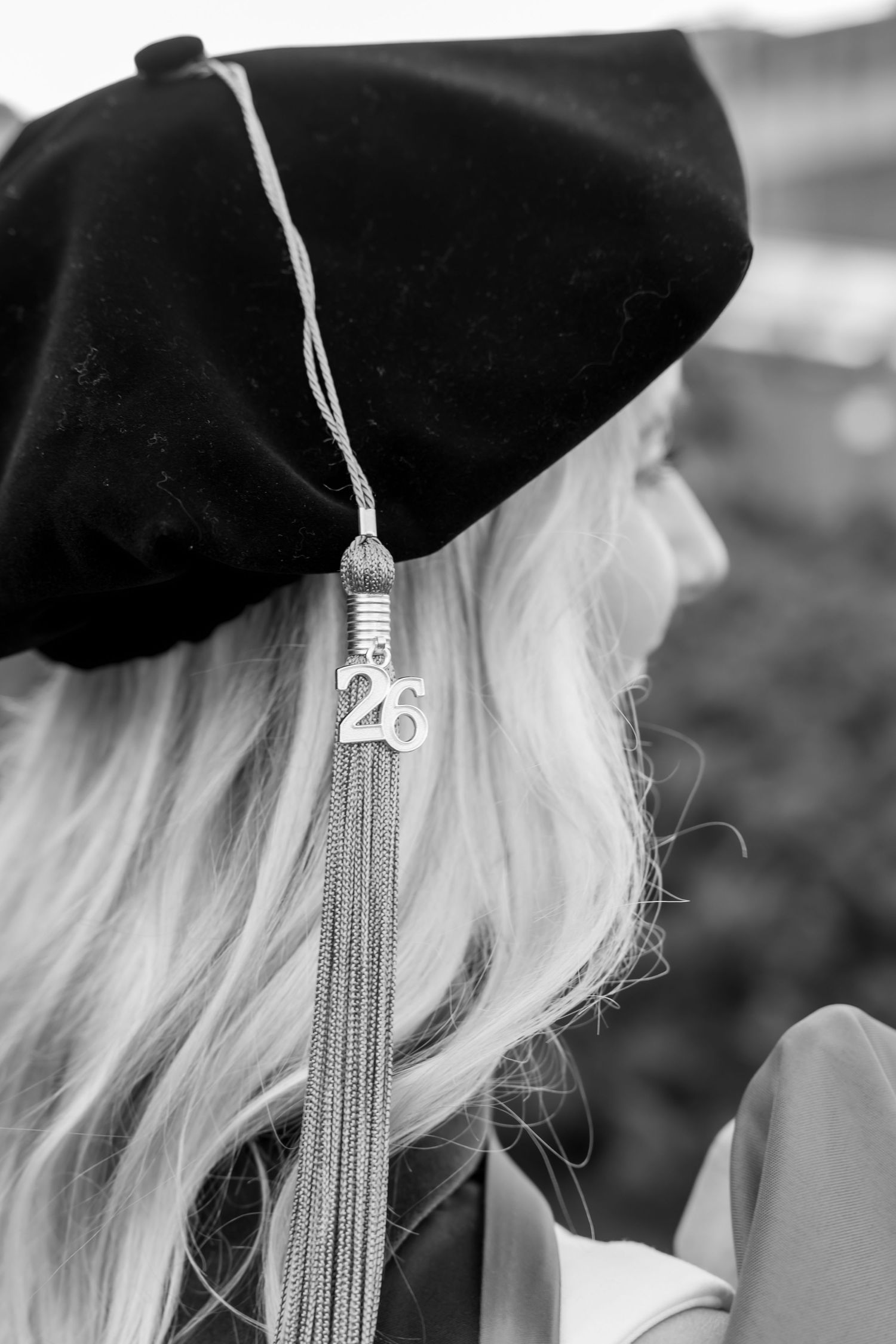 Black and white photo of a graduate wearing a black cap with a tassel charm reading 26, with long blonde hair.
