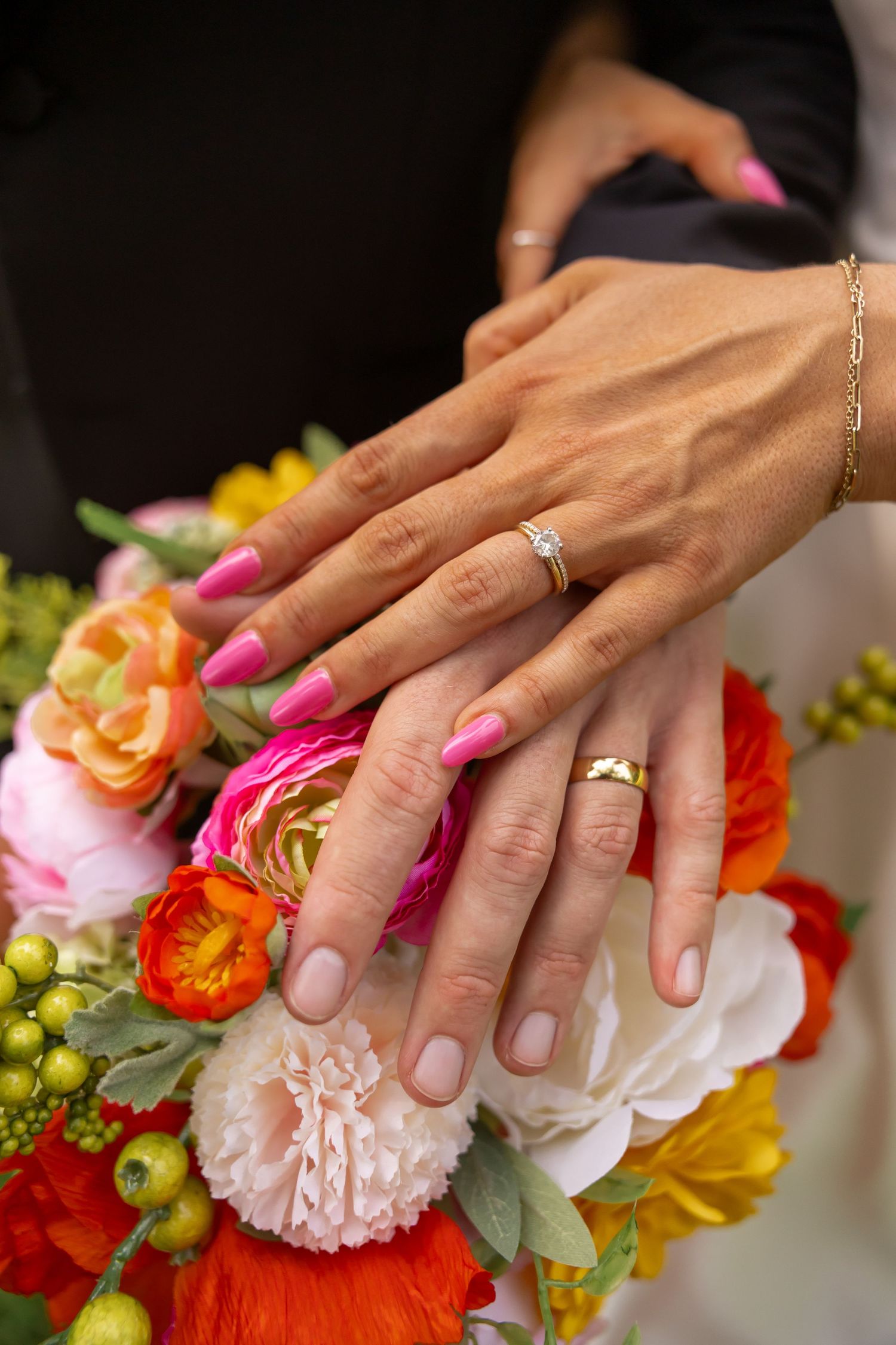 Bride and groom hands with wedding rings resting on colorful bridal bouquet, bride wearing pink manicure.
