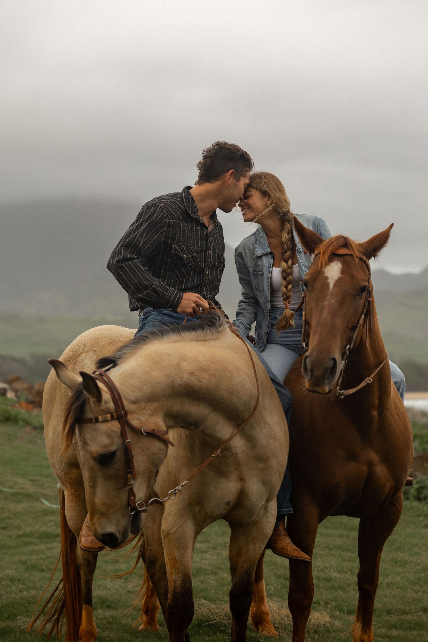 Couple shares romantic moments while sitting on horseback in a misty field.