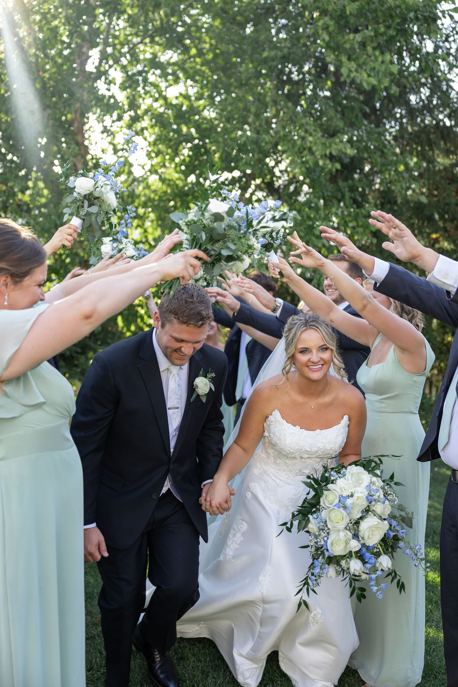 Wedding party strikes fun poses with arms raised in a coordinated group photo.