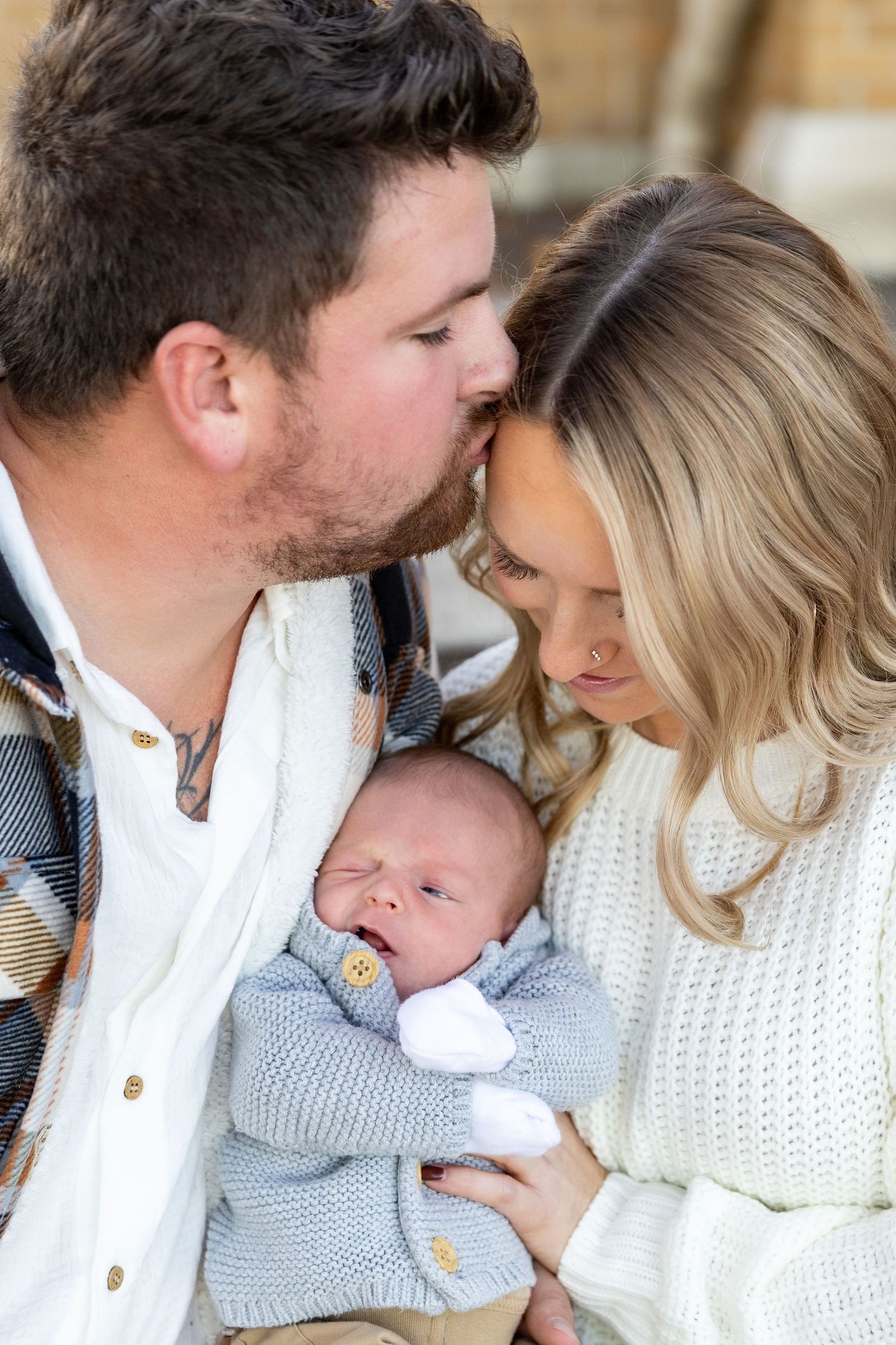 Family snuggling together in cozy white knit sweaters during intimate photo session.