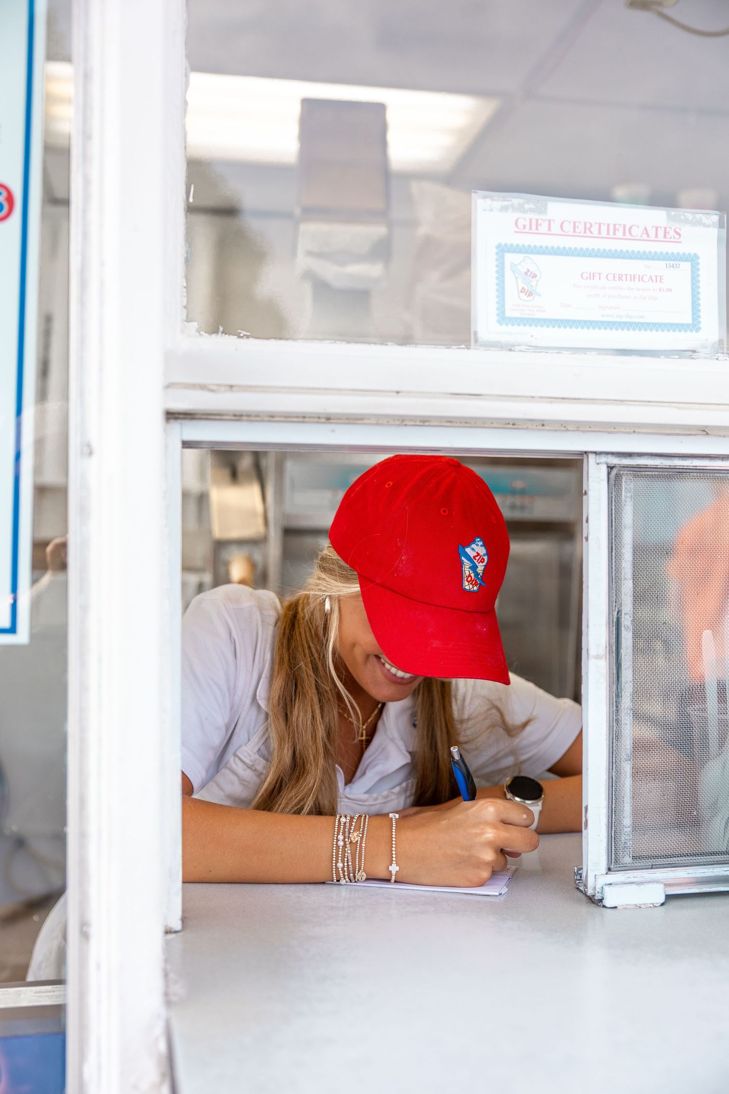 Person in red cap writing or signing documents at service counter window.